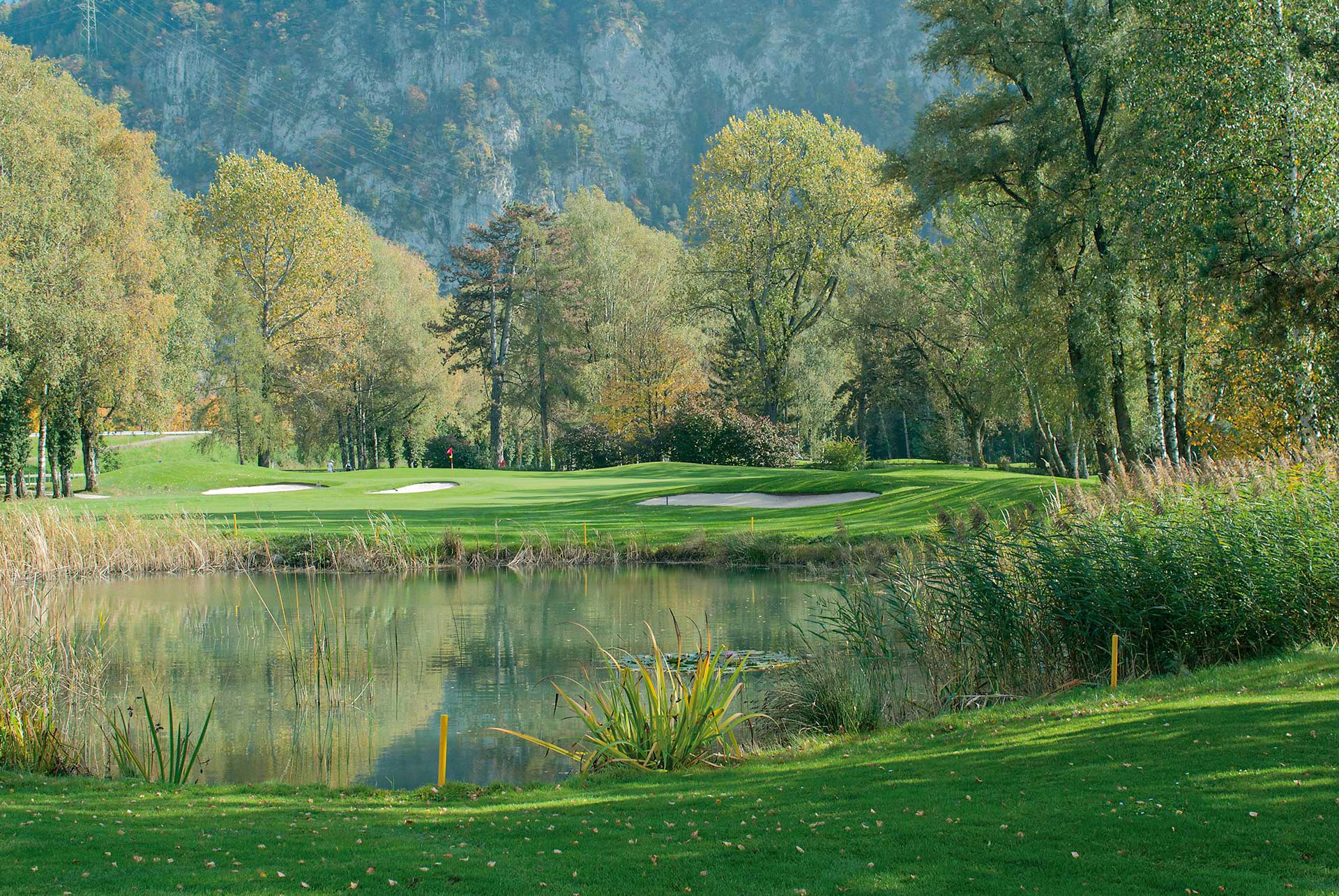 Ein Golfplatz mit einem künstlichem Teich und kurz getrimmtem Rasen mit Bäumen runderherum