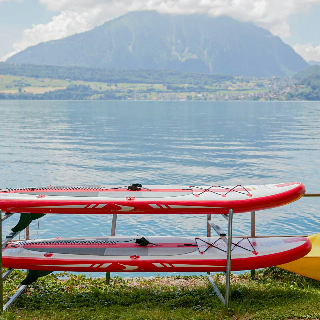 Water sports at Hotel BEATUS Two red SUPs in front of Lake Thun, with a large mountain behind them