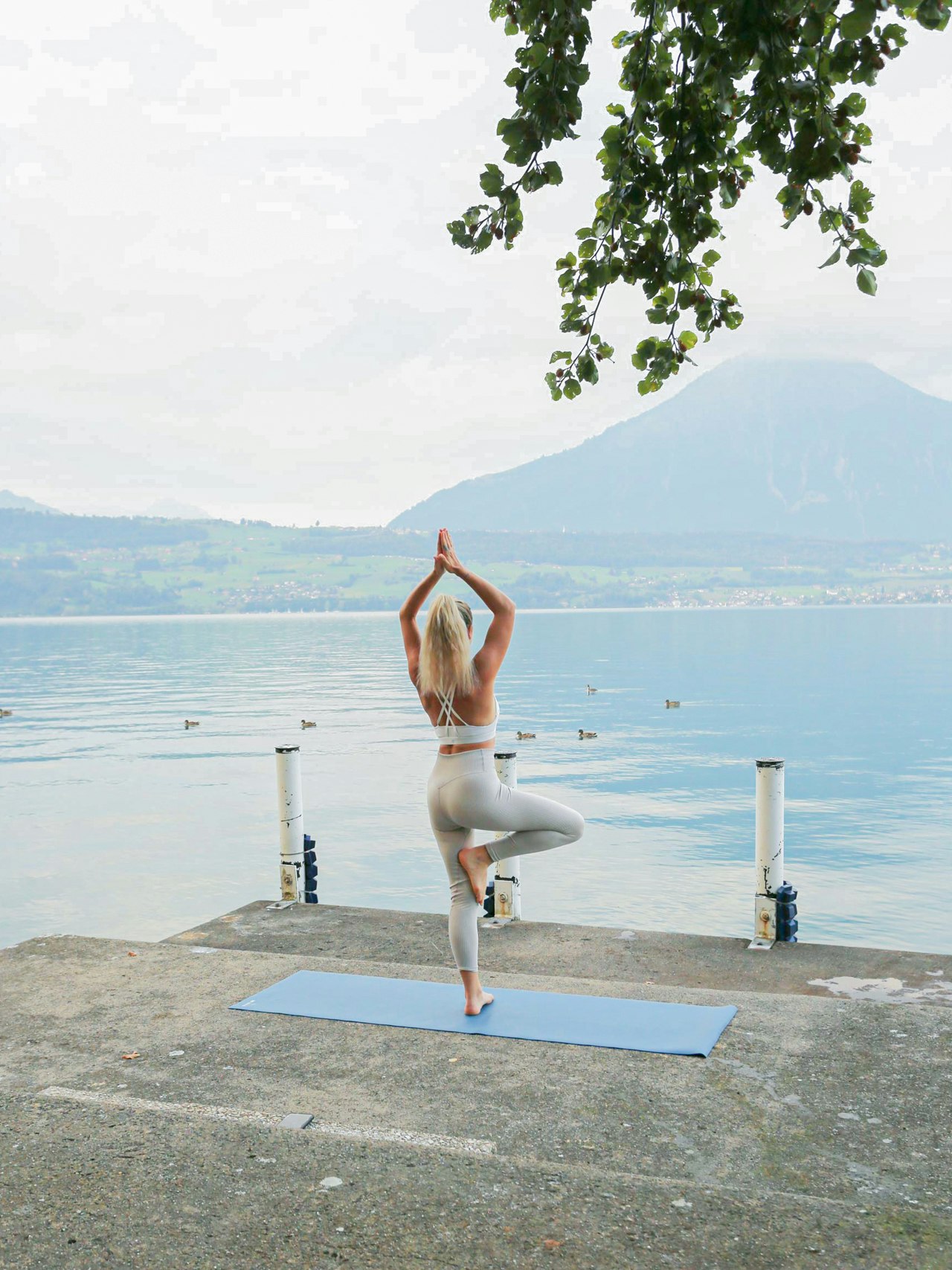 Yoga am See im Hotel BEATUS Eine Frau steht in einer Yogaposition auf einer blauen Yogamatte vor dem Thunersee