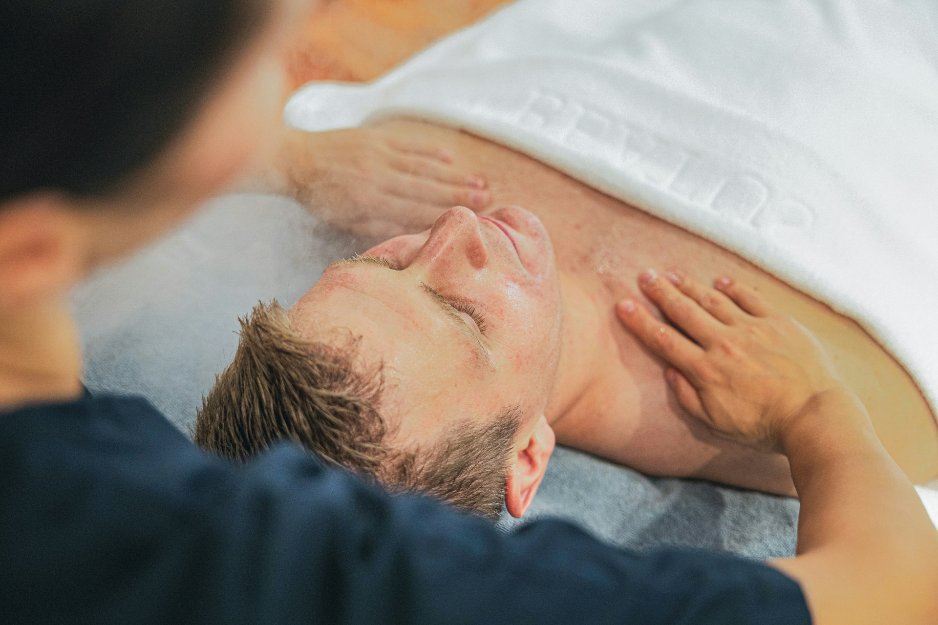 Ein Mann liegt auf dem Rücken auf einer Massageliege und wird an den Schultern massiert