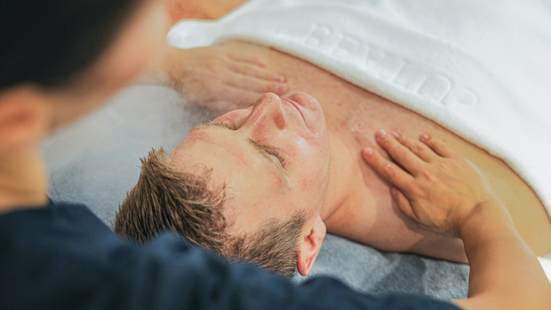 Beautybehandlung im Hotel BEATUS Ein Mann liegt auf dem Rücken auf einer Massageliege und wird an den Schultern massiert