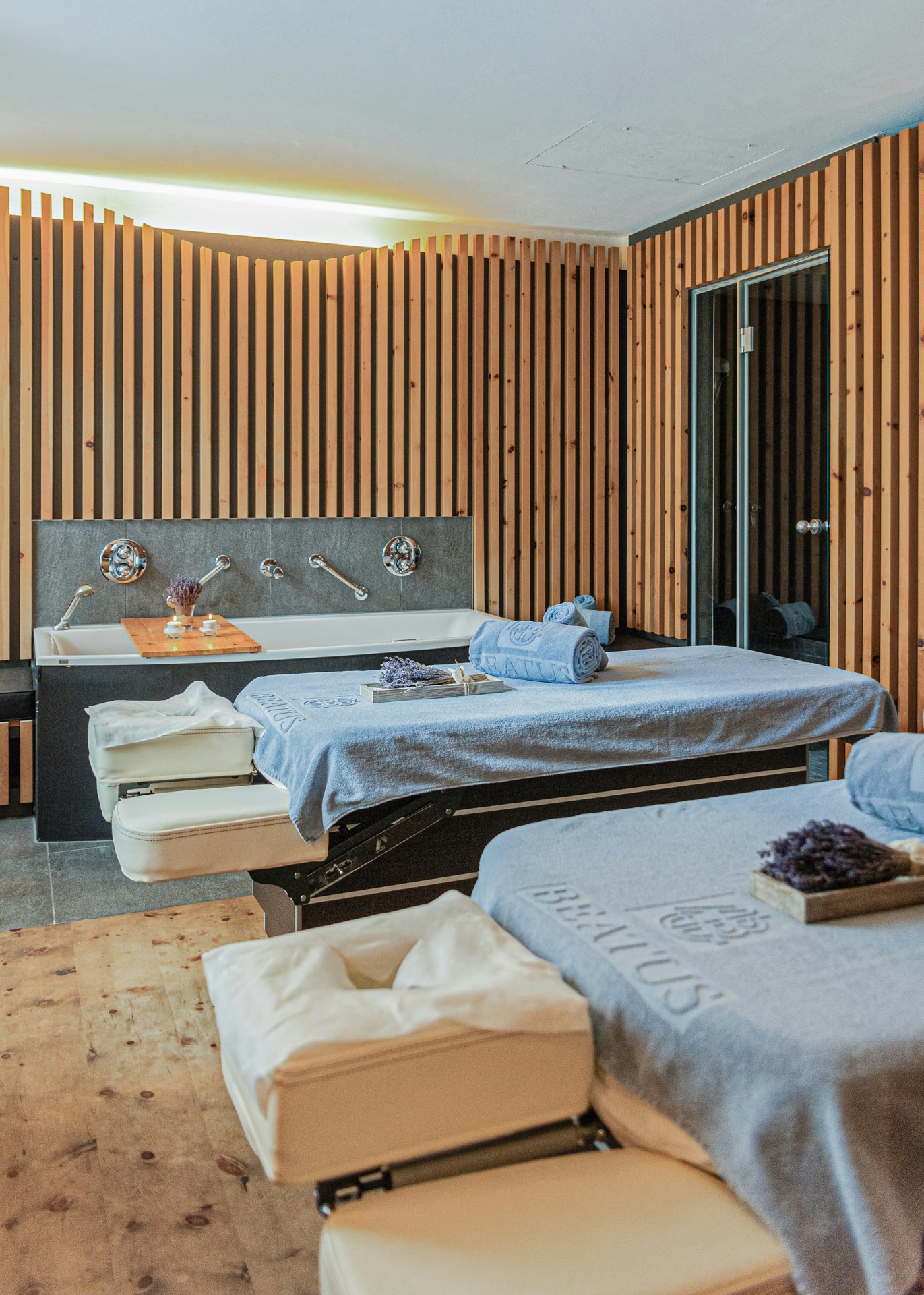 Zwei Massageliegen mit Badetüchern in einem Raum mit Holzlatten vor den Wänden