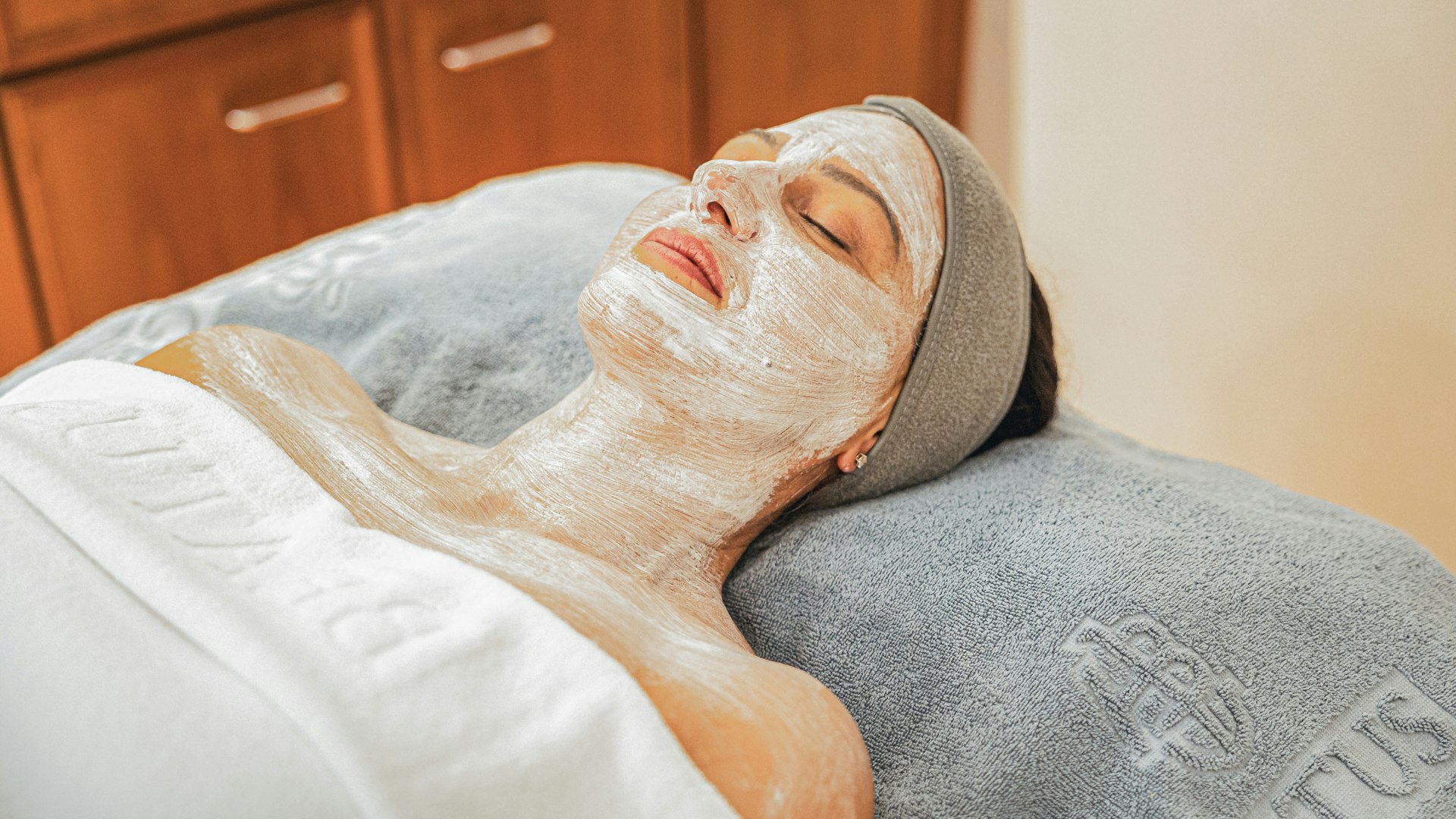 Beauty treatments at the Hotel BEATUS Woman with a cosmetic mask on her face lies on a massage bench, covered by a white towel, with a blue towel underneath her