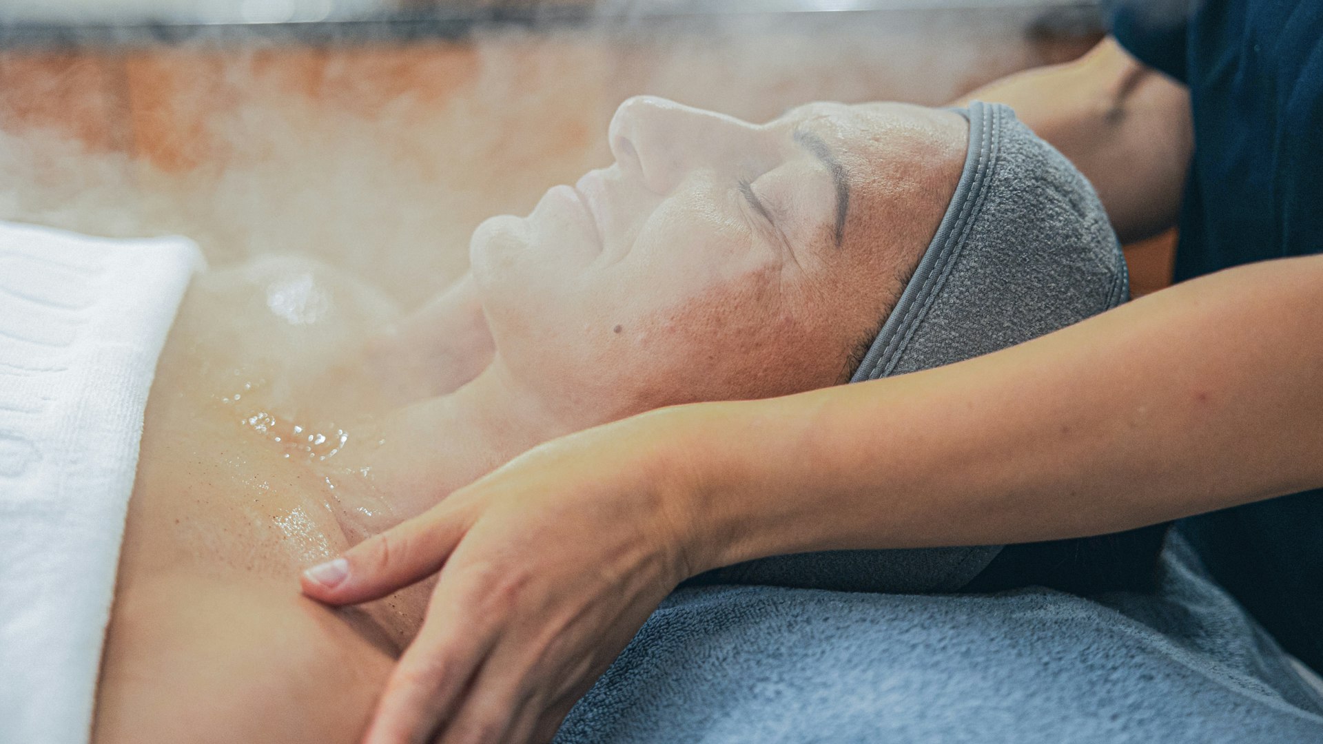 Beauty treatments at the Hotel BEATUS A woman lies on a massage table, her face in the steam, behind her a masseuse massaging her shoulders
