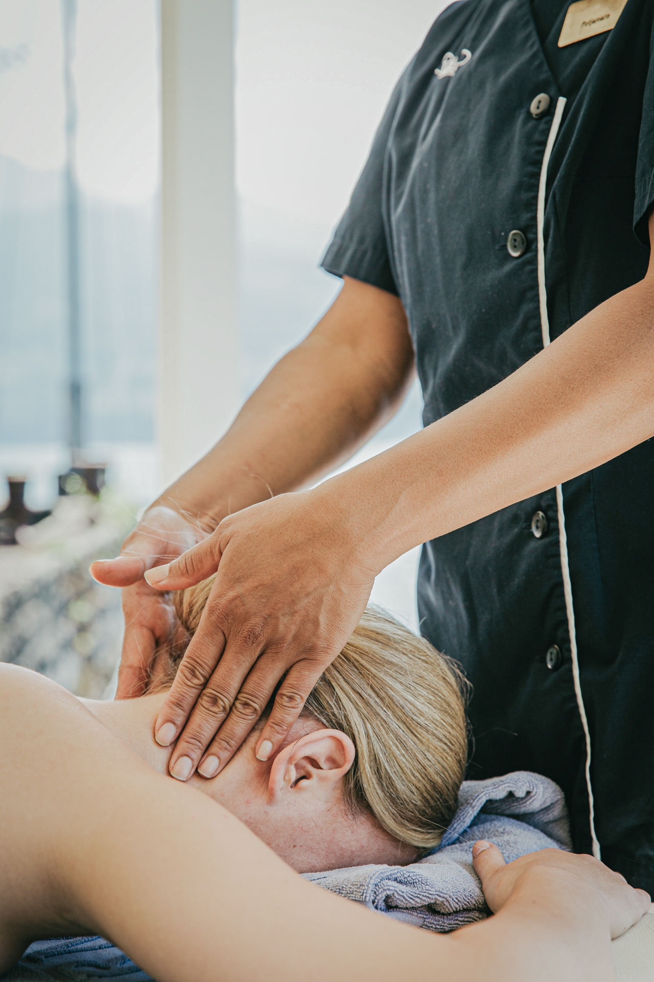 Eine Frau liegt auf dem Bauch, ihr Nacken wird massiert, dahinter der See