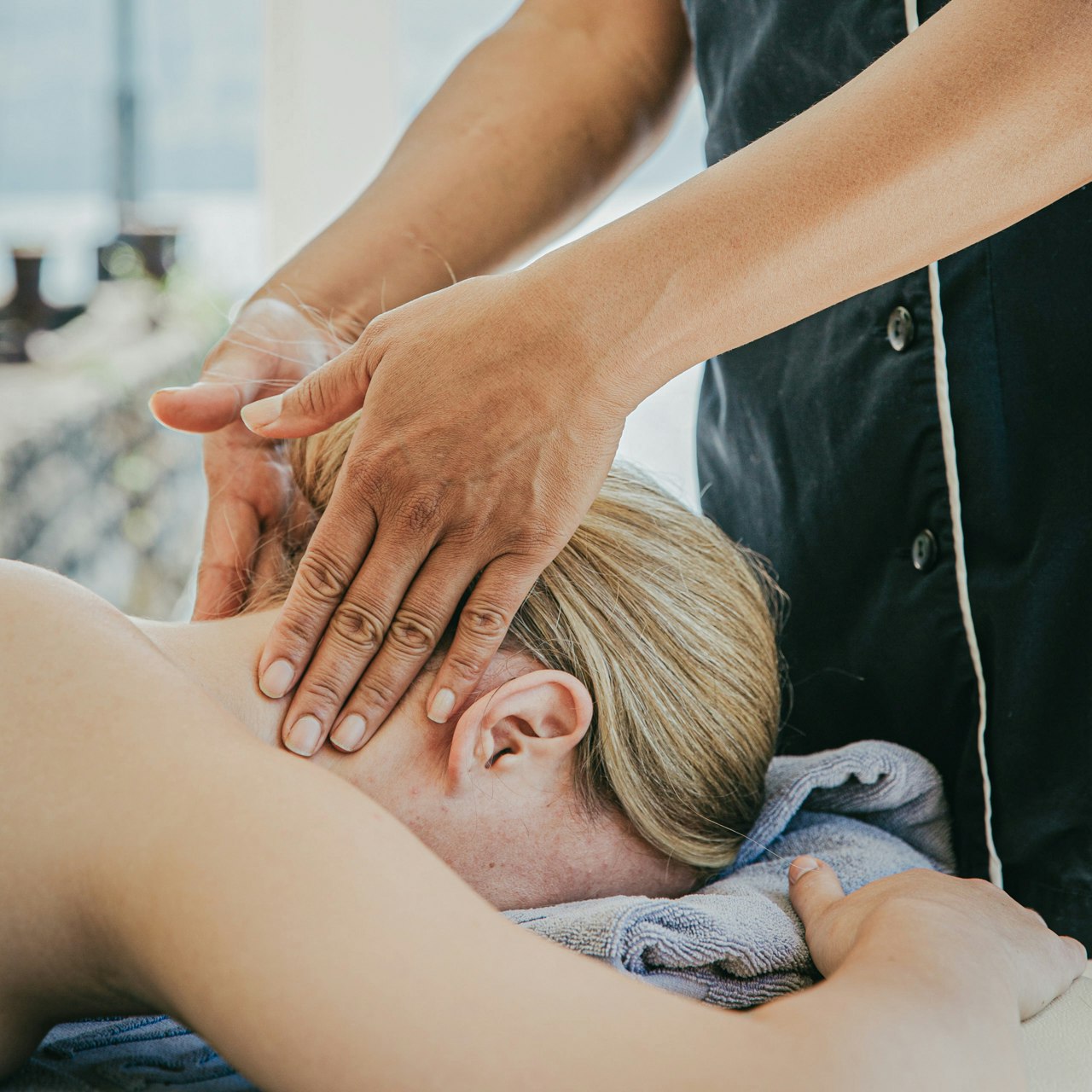 Massage am See im Hotel BEATUS Eine Frau liegt auf dem Bauch, ihr Nacken wird massiert, dahinter der See