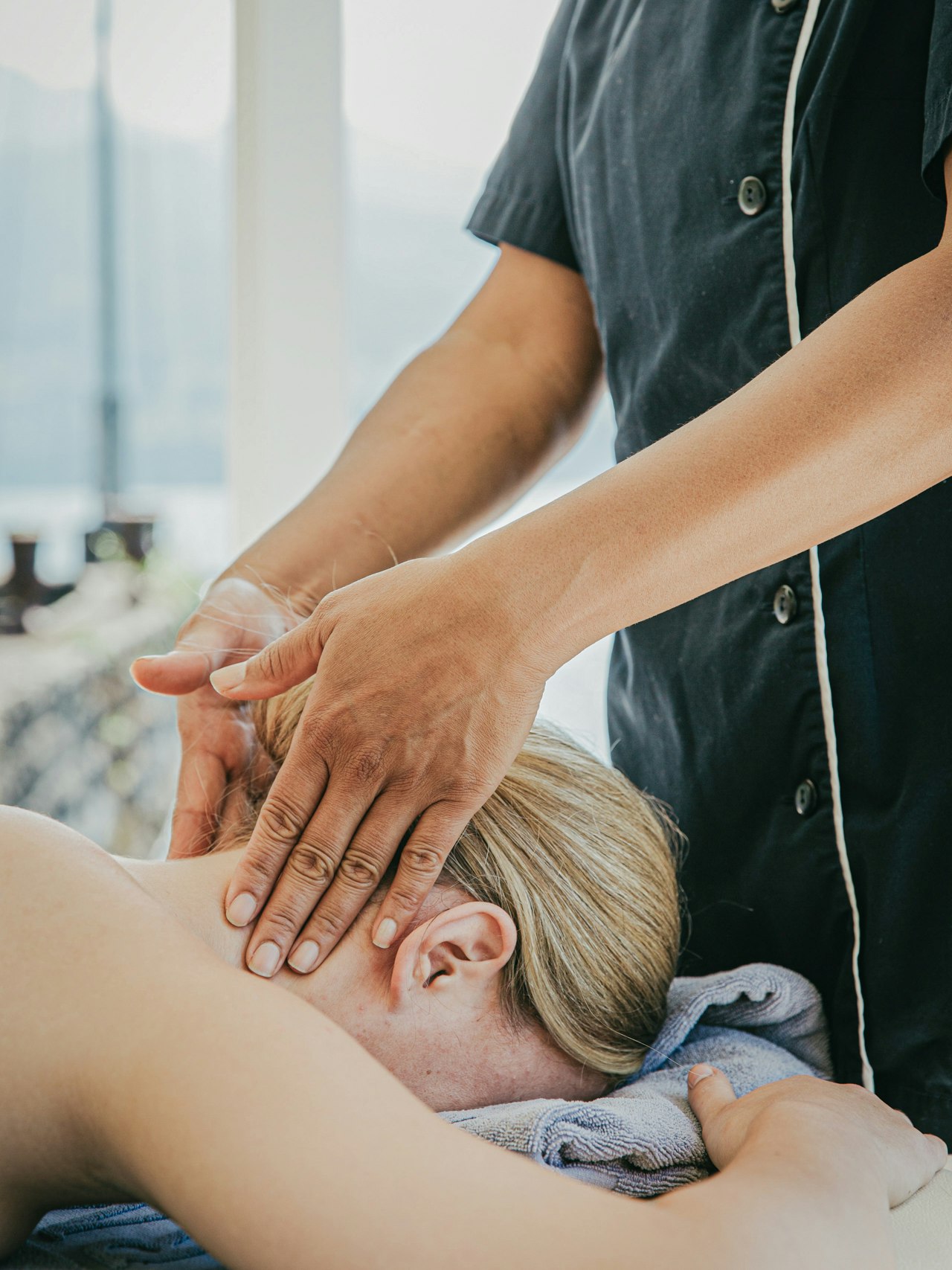Massage am See im Hotel BEATUS Eine Frau liegt auf dem Bauch, ihr Nacken wird massiert, dahinter der See