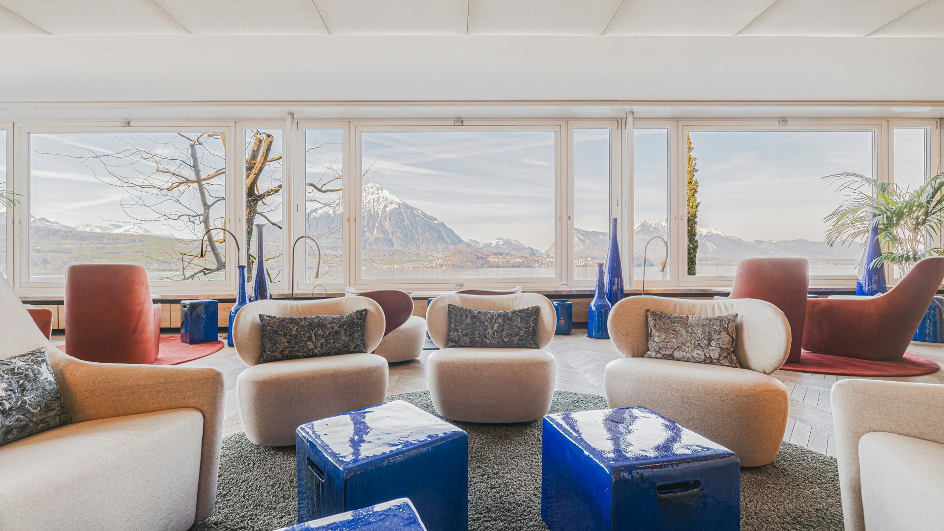 Lobby at the Hotel BEATUS White sofa and upholstered furniture, blue tables in front of it, view of the lake from a large panoramic window