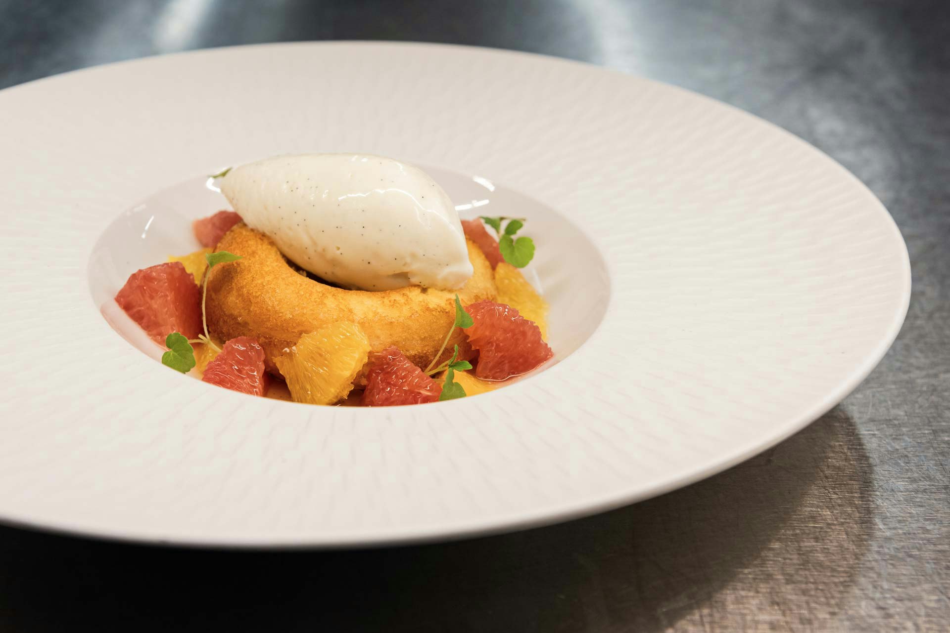 Assiette blanche sur fond métallique, avec des filets d'orange, un cercle de pâte et de la glace à la vanille