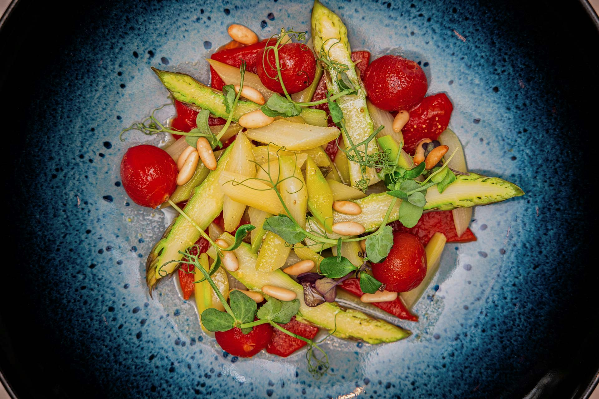 Blauer Teller mit gekochten Tomaten und Spargeln