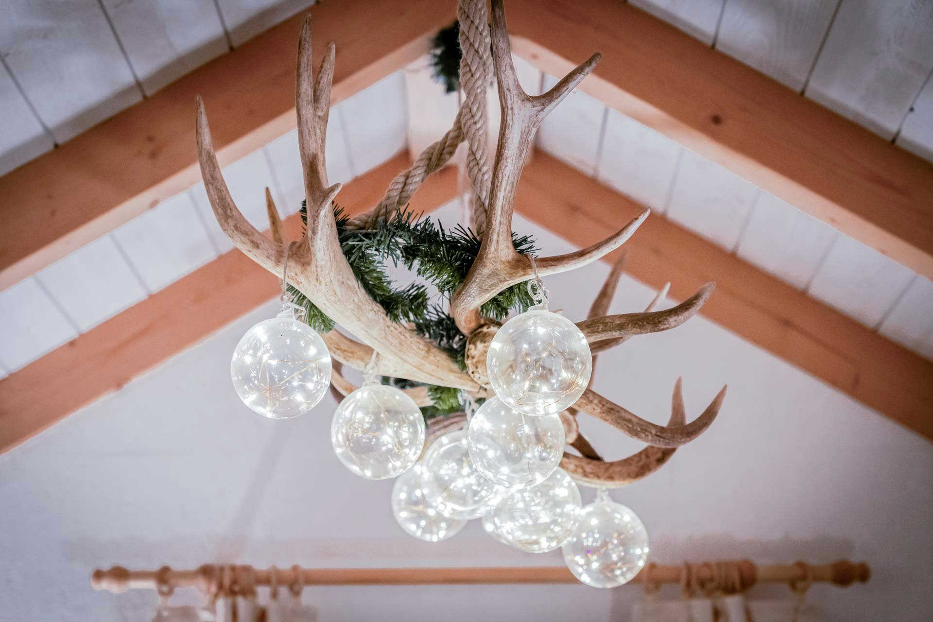 Ceiling light made of deer antlers, twigs and glass balls, on a gabled wooden ceiling
