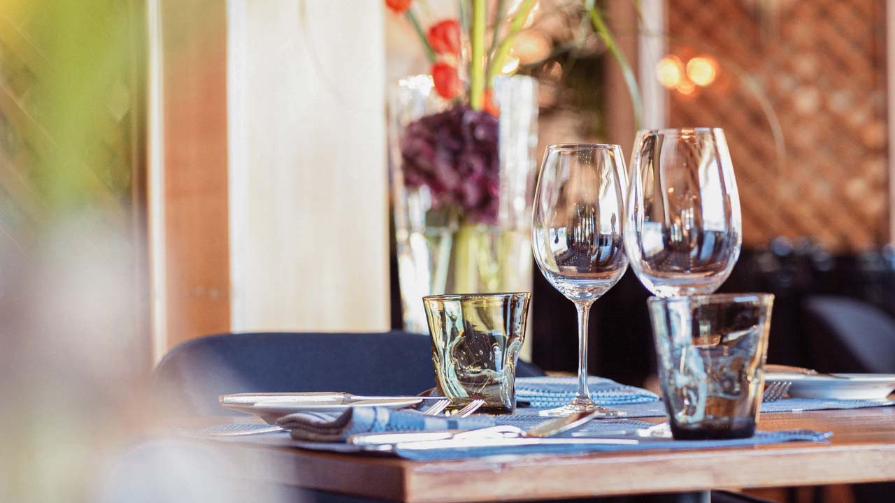 Restaurant Orangerie de l'hôtel BEATUS Chaises noires rembourrées autour d'une table dressée, derrière un revêtement en bois brun miel et des fleurs