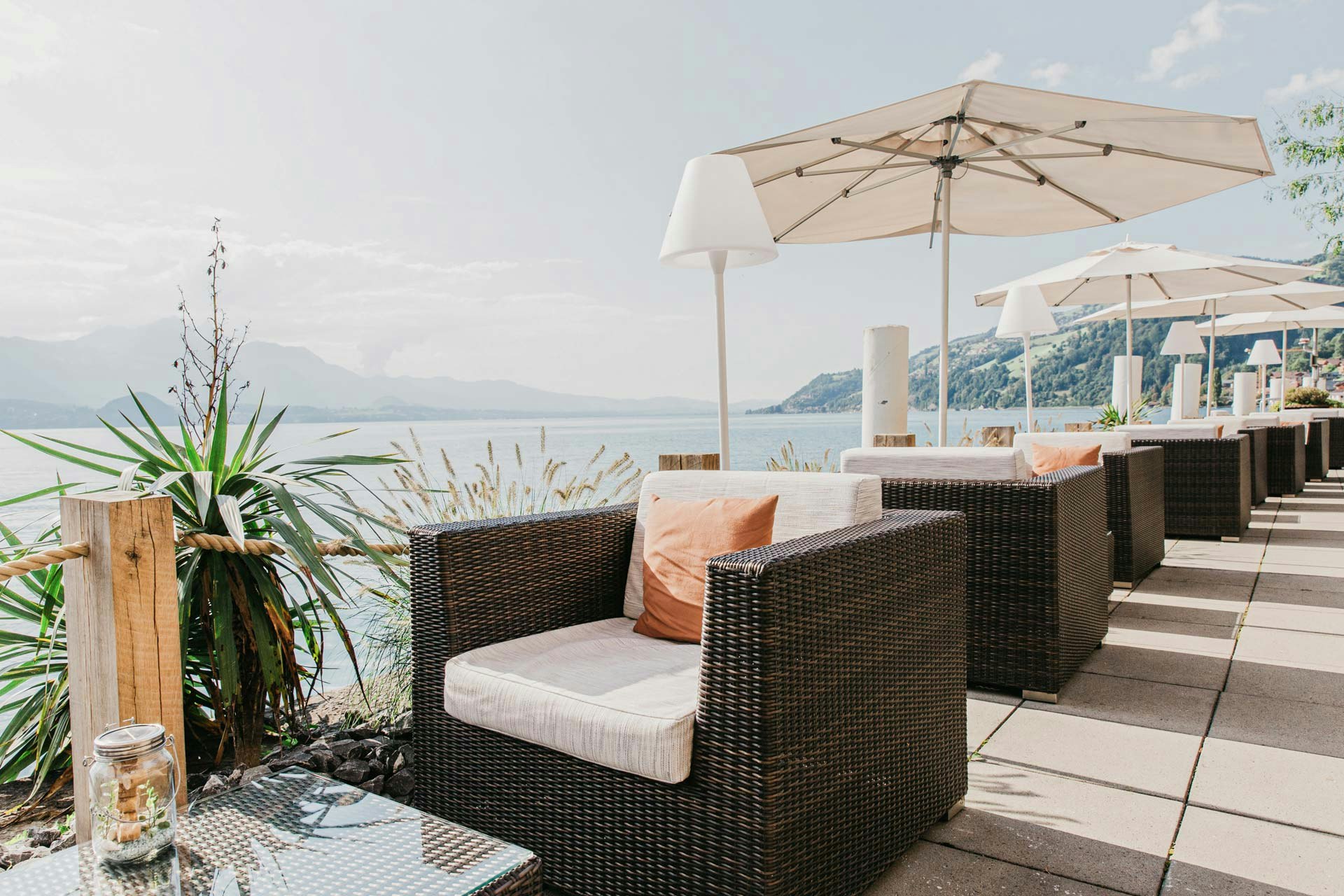 Meubles de salon, parasols et lampadaires sur une terrasse, à gauche le lac