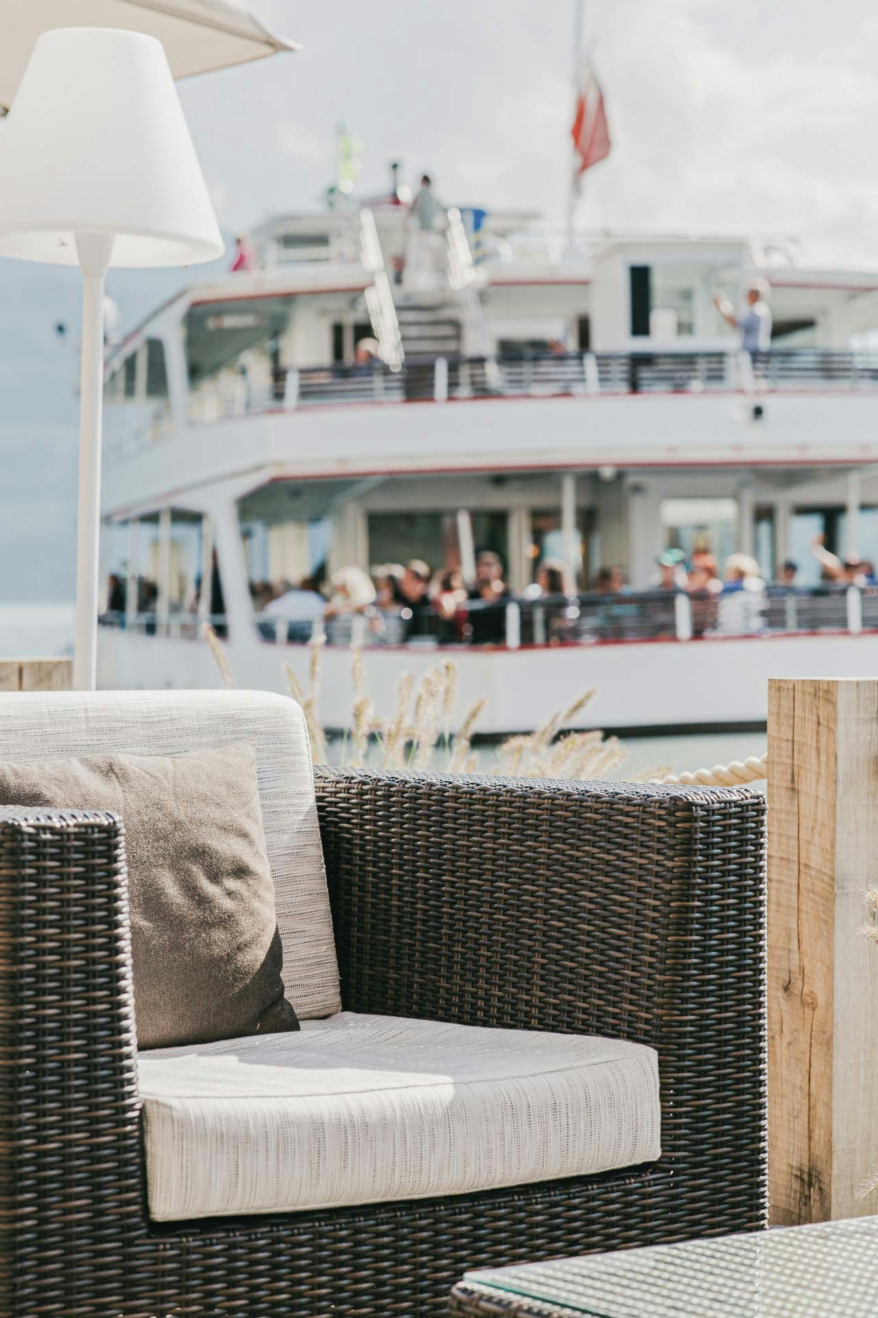Meubles de salon et lampadaire, derrière, dans le flou, un bateau de plaisance avec des personnes en gros plan