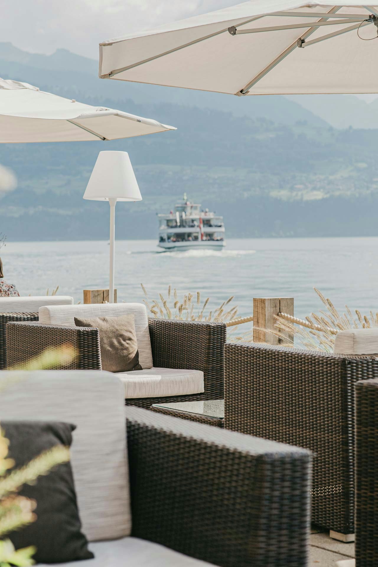 Meubles de salon tressés, parasols et lampadaire blanc, derrière le lac avec un bateau d'excursion et une montagne