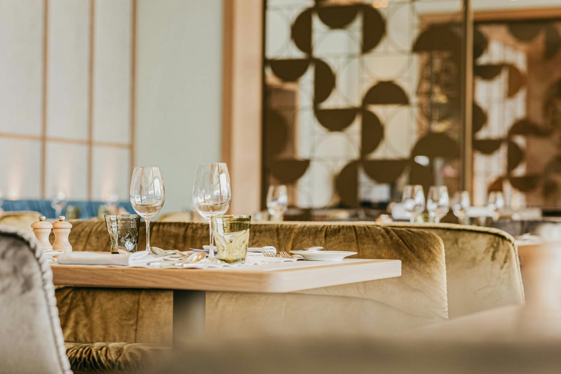 Velvet-covered chairs, behind them an artistic partition wall made of golden metal, on the right a large panoramic window with a view of the lake