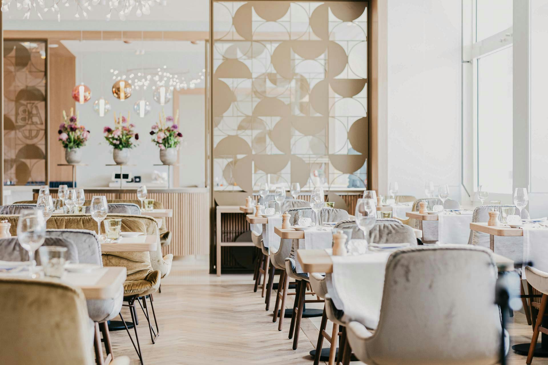 Velvet-covered chairs, behind them an artistic partition wall made of golden metal, on the right a large panoramic window with a view of the lake