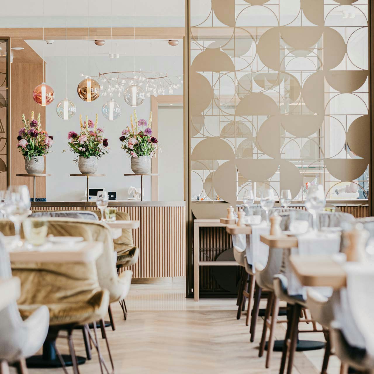 Table d'hôte im Hotel BEATUS Mit Samt überzogene Stühle, dahinter eine kunstvolle Trennwand aus goldenem Metall, Blumen