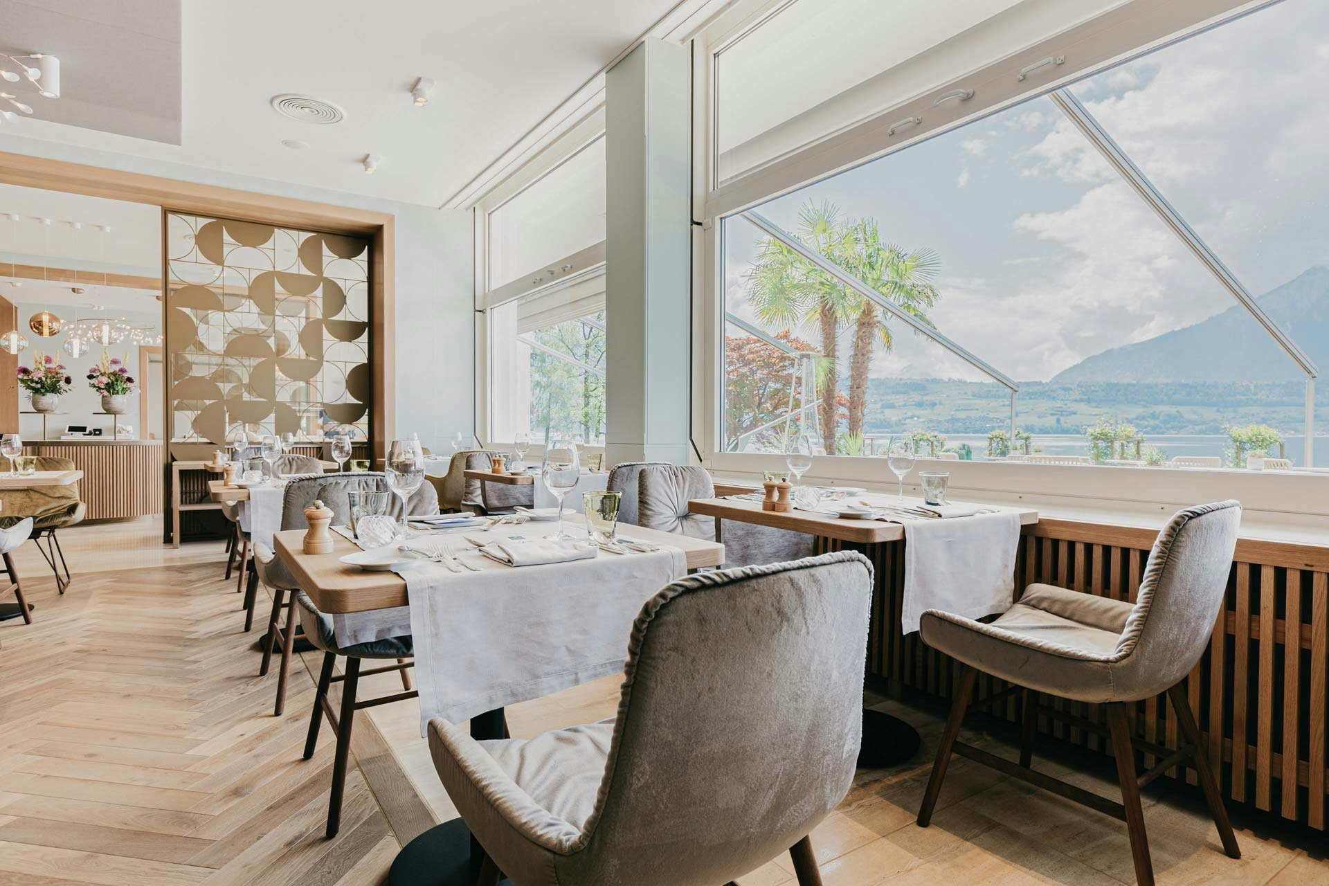 Velvet-covered chairs, behind them an artistic partition wall made of golden metal, on the right a large panoramic window with a view of the lake