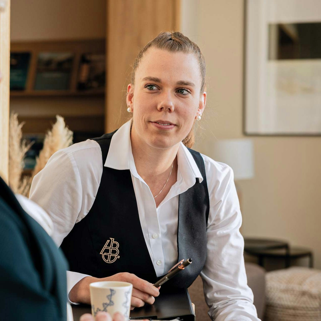 Martina Kohli bei der Arbeit im Hotel BEATUS Freundliche Frau mit weissem Hemd und schwarzem Gilet im Kundenkontakt