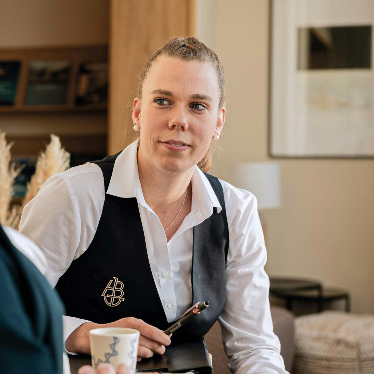 Martina Kohli au travail à l'hôtel BEATUS Une femme aimable en chemise blanche et gilet noir en contact avec la clientèle
