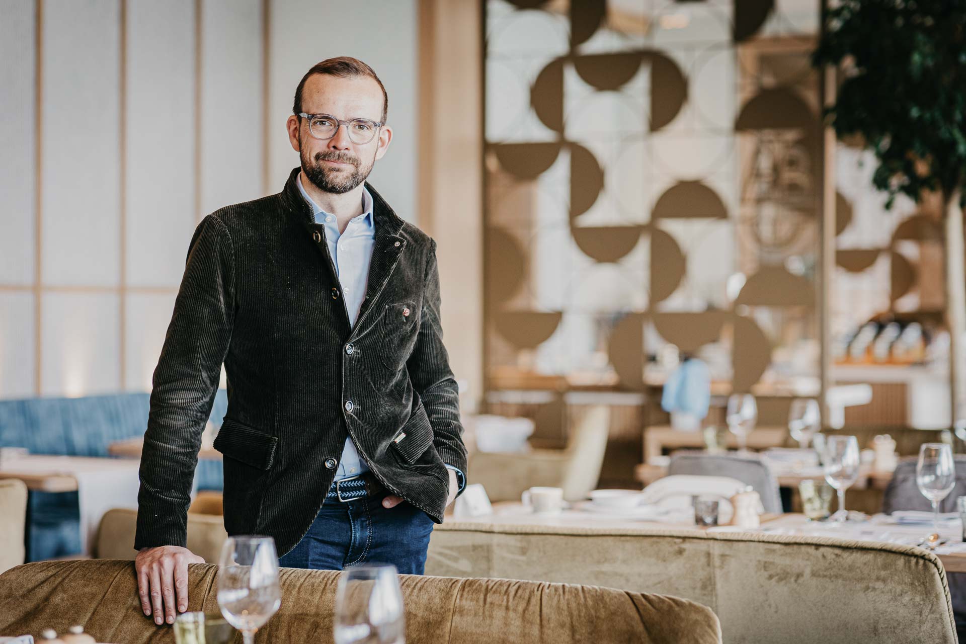 Salopp gekleideter Mann mit Brille und Bart in einem Restaurant, eine Hand in der Hosentasche