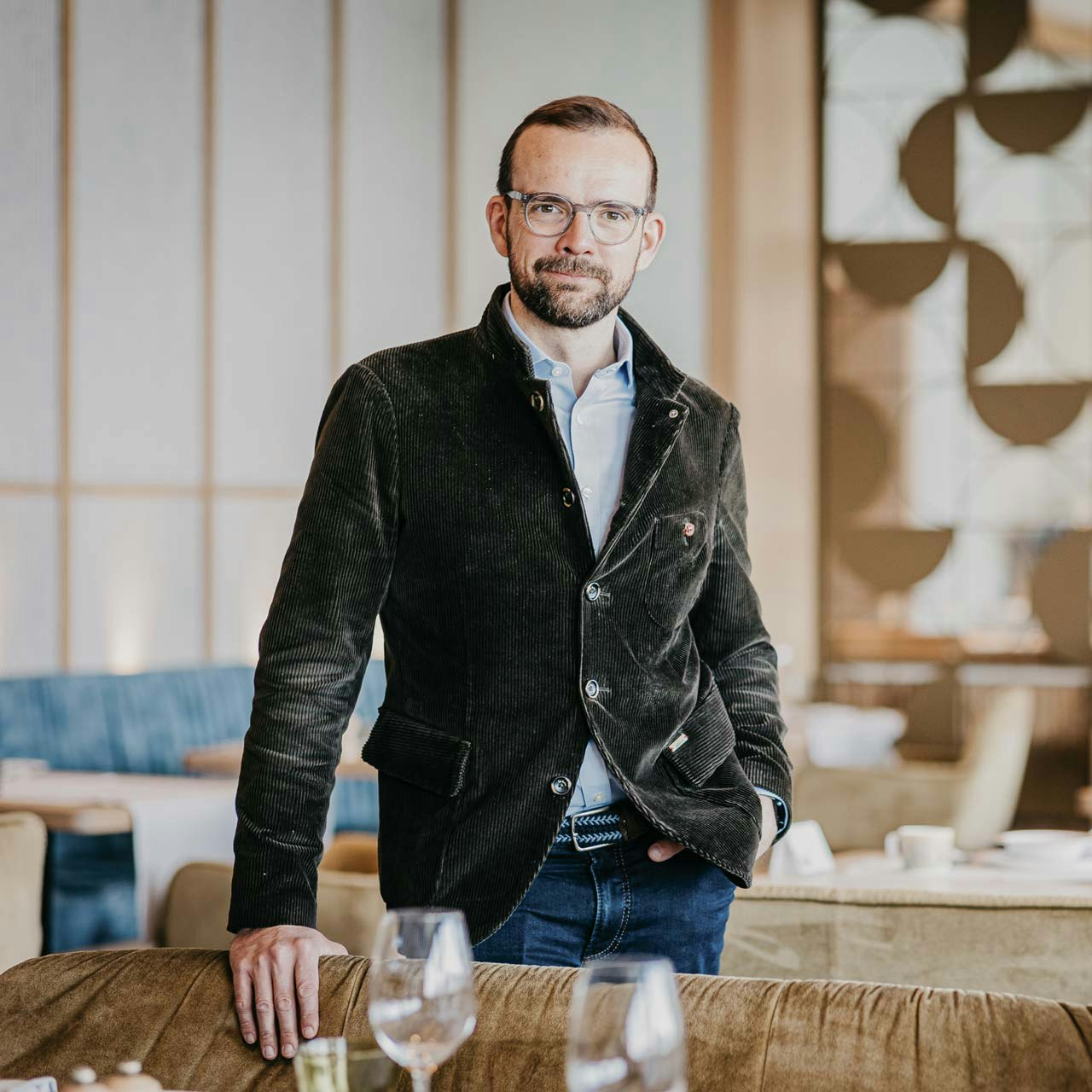 Sebastian Moser, General Director Hotel BEATUS Casually dressed man with glasses and beard in a restaurant, one hand in his trouser pocket
