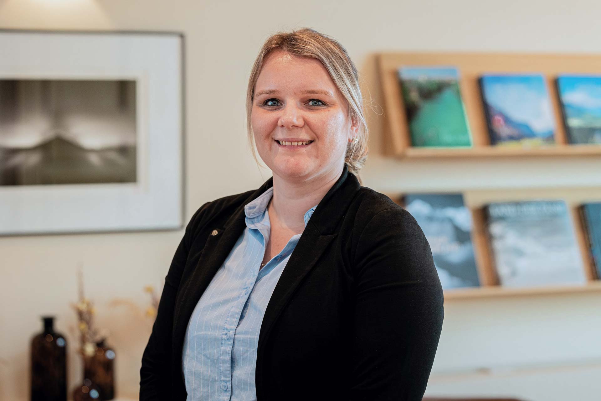 Frau mit blauer Bluse und schwarzer Weste vor Regal mit Magazinen