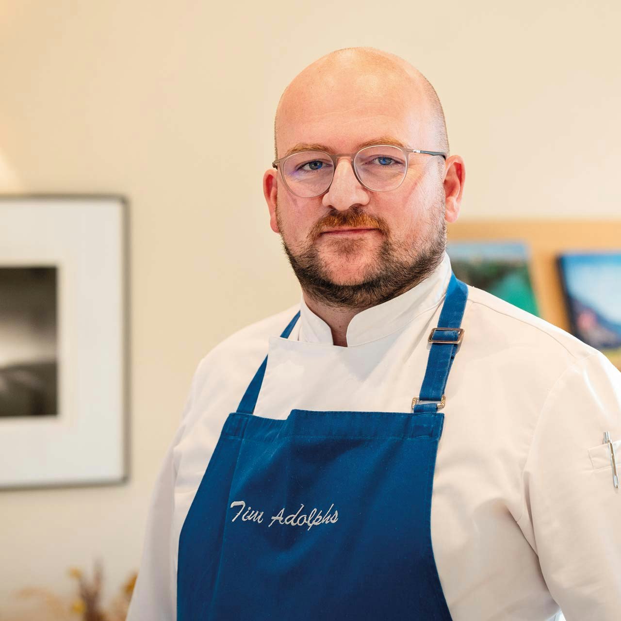 Tim Adolphs, head chef at Hotel BEATUS Bearded man with glasses, white shirt and blue apron