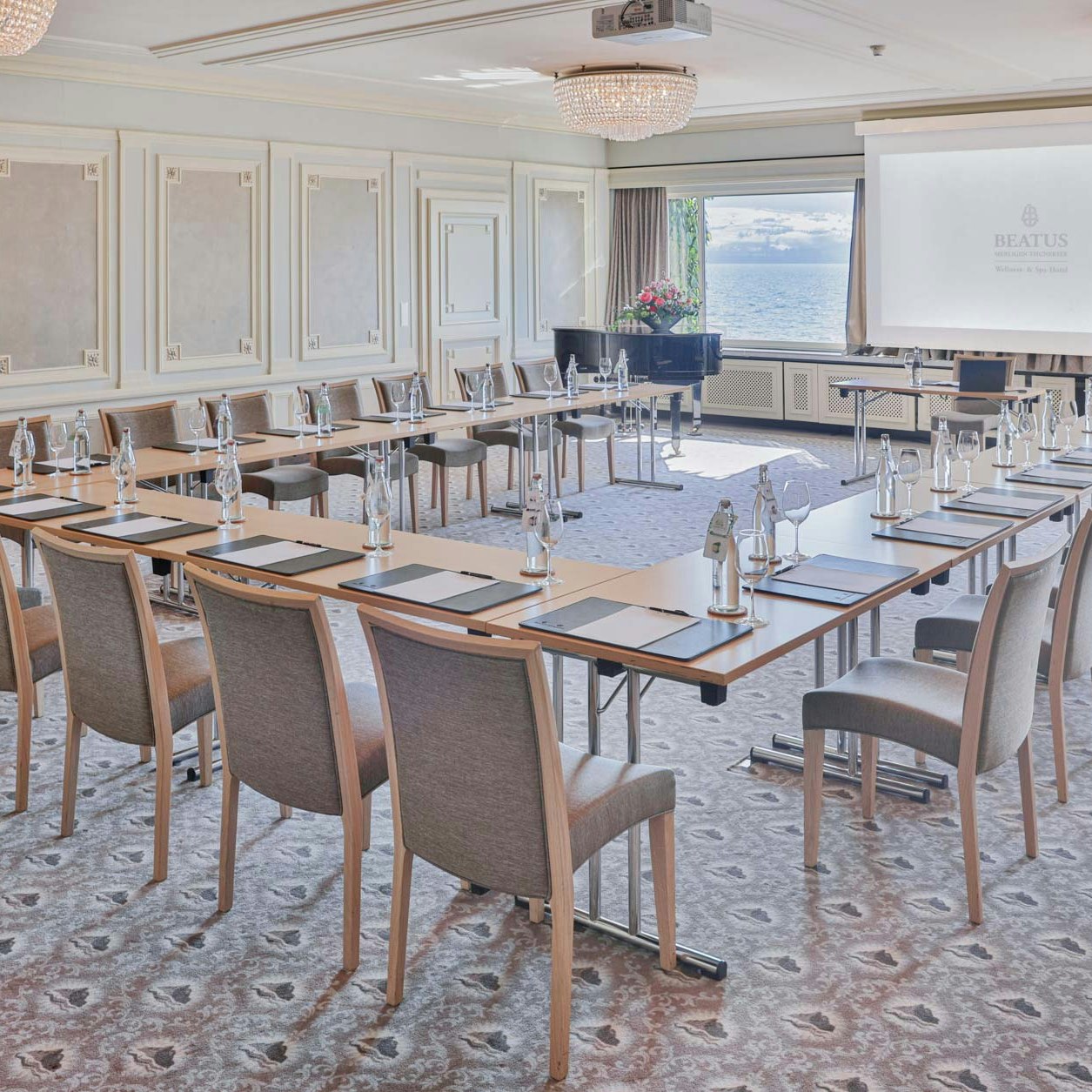 Seminar room at Hotel BEATUS Large room with patterned carpet, round crystal patterns, white wood panelling and large panoramic windows, tables and chairs in the centre, flipchart at the front
