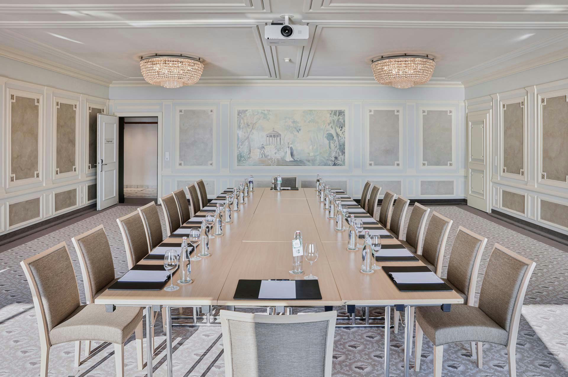 Grande salle avec moquette à motifs, motifs ronds en cristal, boiseries blanches et tableau romantique, au centre tables et chaises