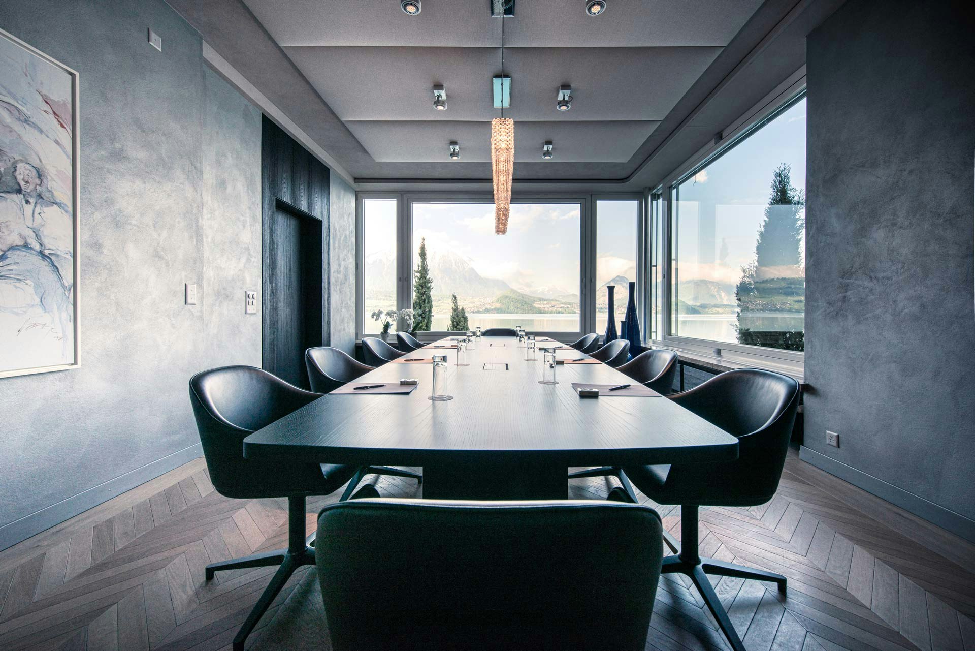 Salle aux murs sombres, au centre une grande table et des chaises de bureau noires tout autour, grande fenêtre avec vue sur le lac