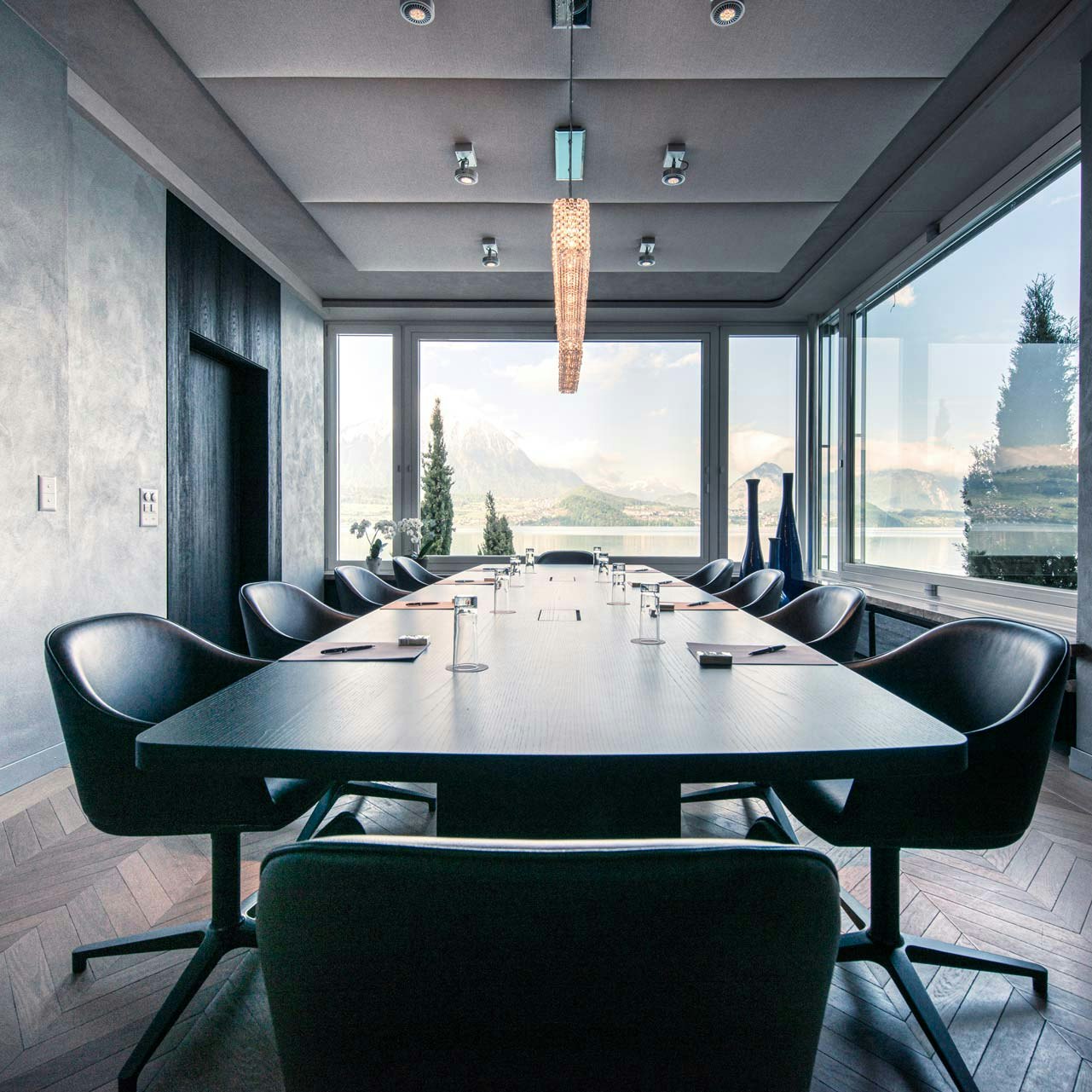 Seminar room at Hotel BEATUS Room with dark walls, a large table in the centre and black office chairs all around, large window with a view of the lake