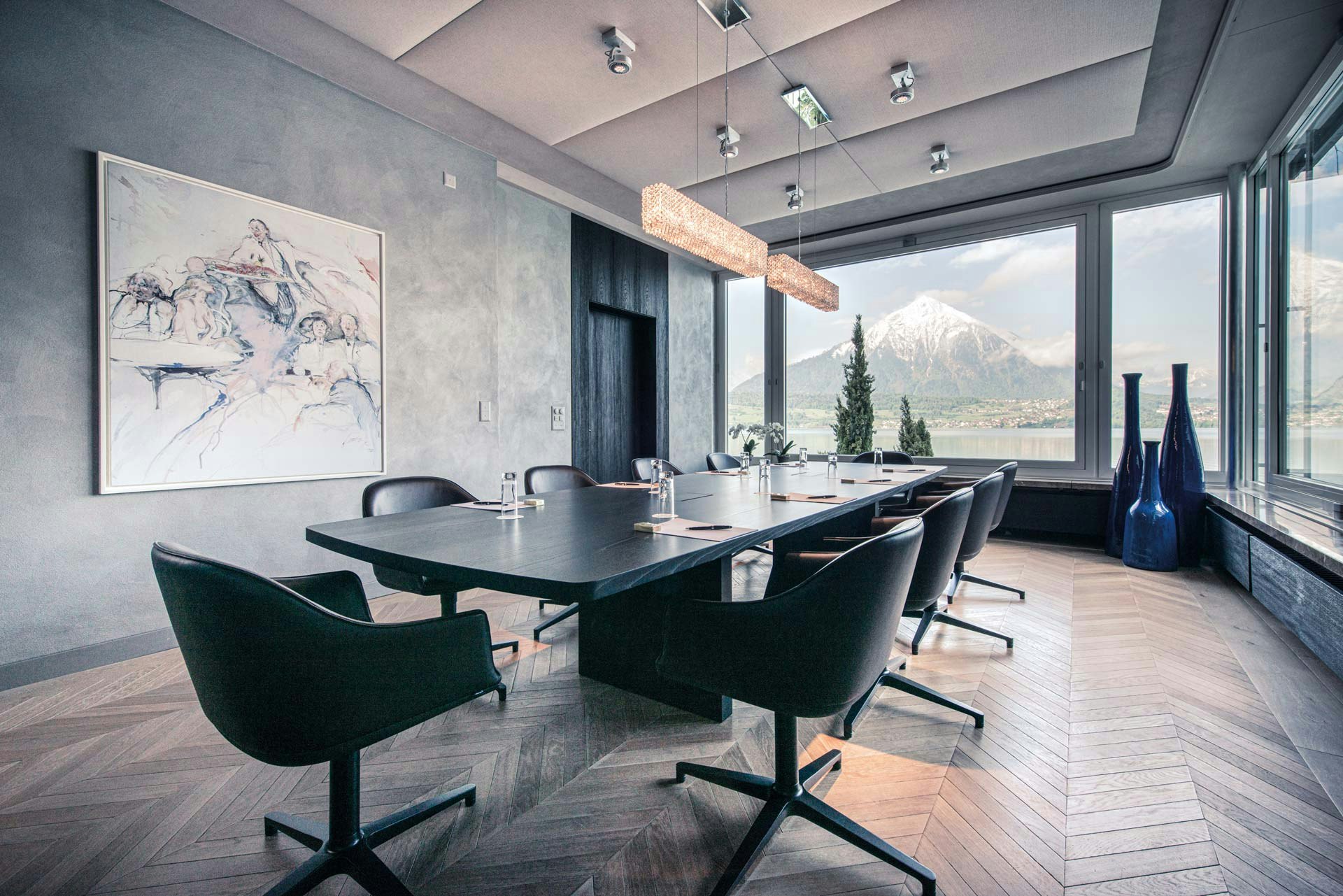 Salle aux murs sombres, au centre une grande table et des chaises de bureau noires tout autour, grande fenêtre avec vue sur le lac