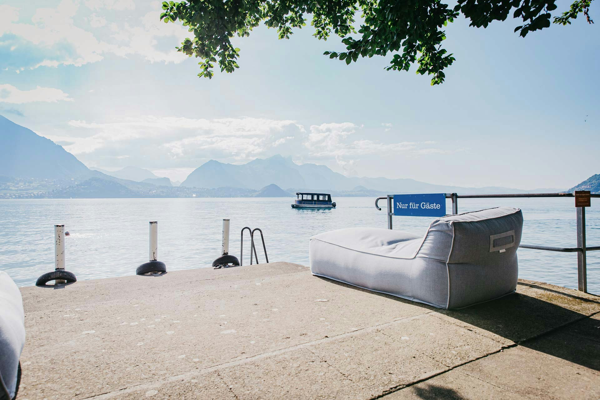 Steg mit Aufschrift «nur für Gäste», darauf ein Polstermöbel, dahinter der See und ein kleines Ausflugsschiff