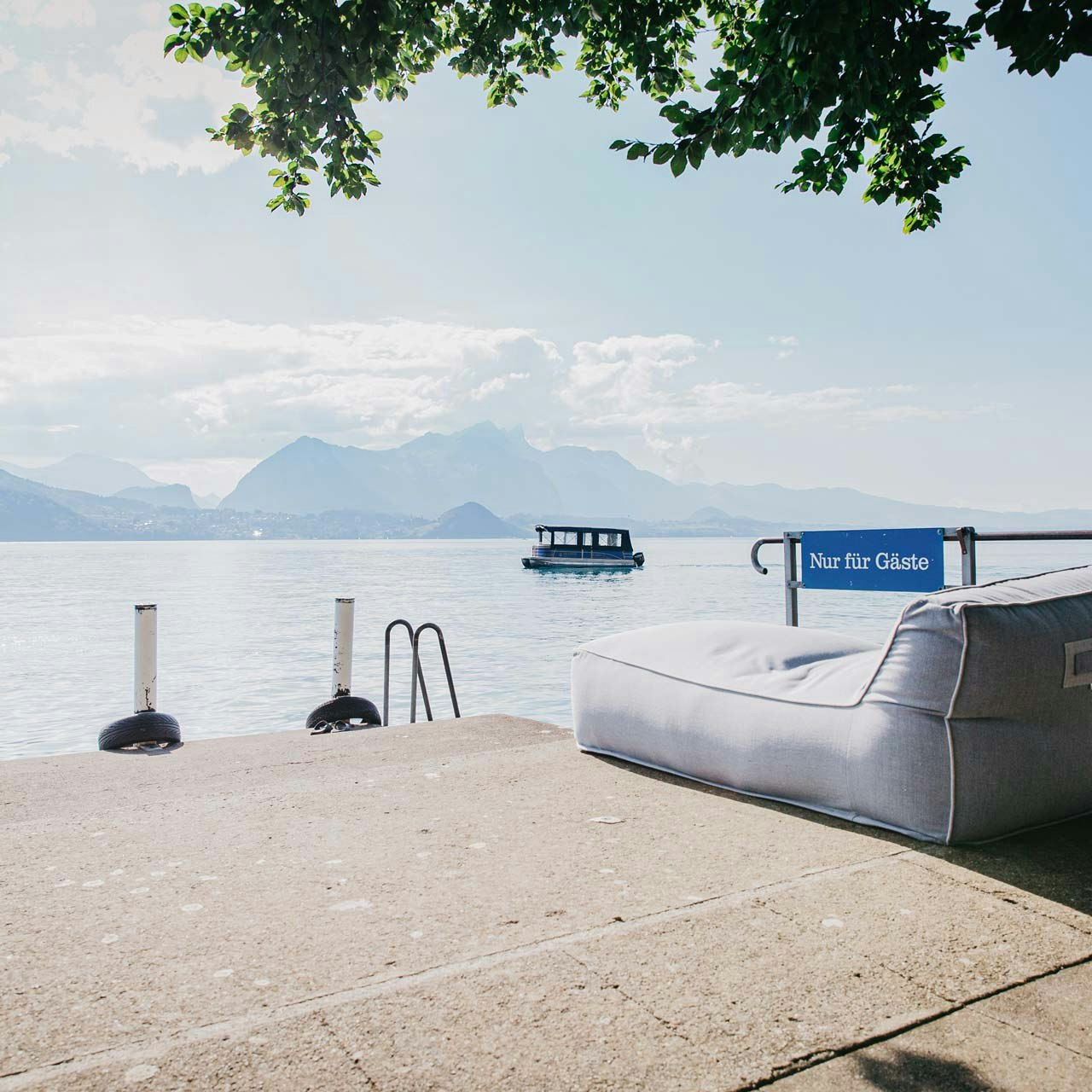 Steg für die Gäste des Hotel BEATUS Steg mit Aufschrift «nur für Gäste», darauf ein Polstermöbel, dahinter der See und ein kleines Ausflugsschiff