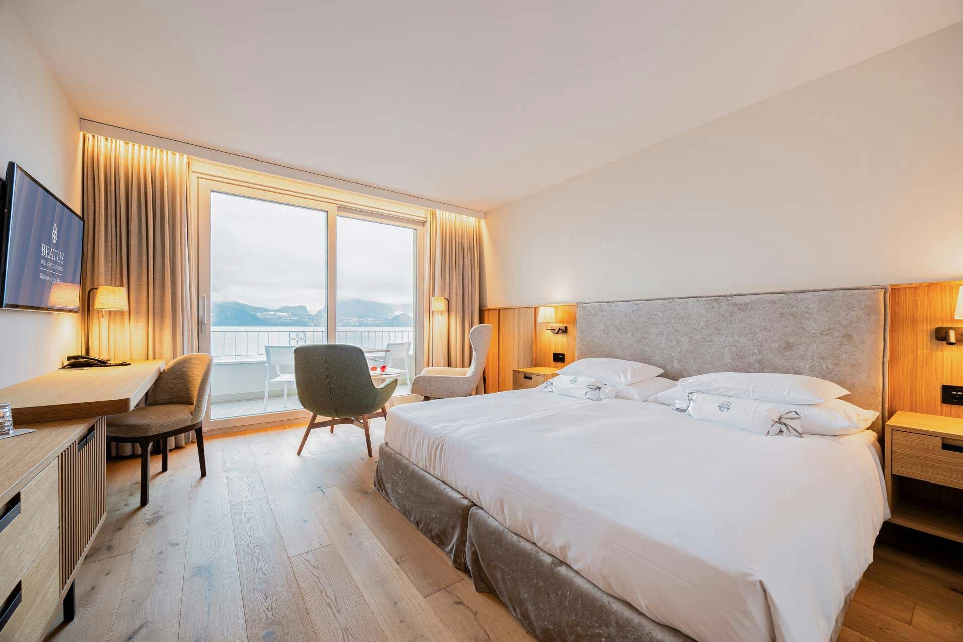 Chambre avec parquet, lit double, table, chaises et fenêtre panoramique sur le balcon