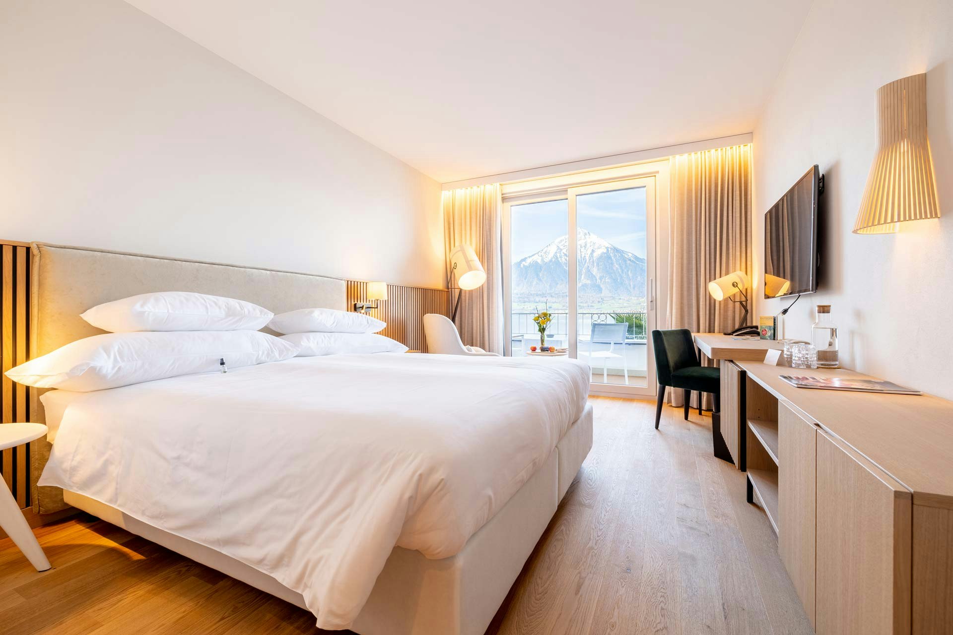 Zimmer mit Parkettboden, Doppelbett, Holzkorpus, Schreibtisch und Stuhl, grosse Glastür zum Balkon