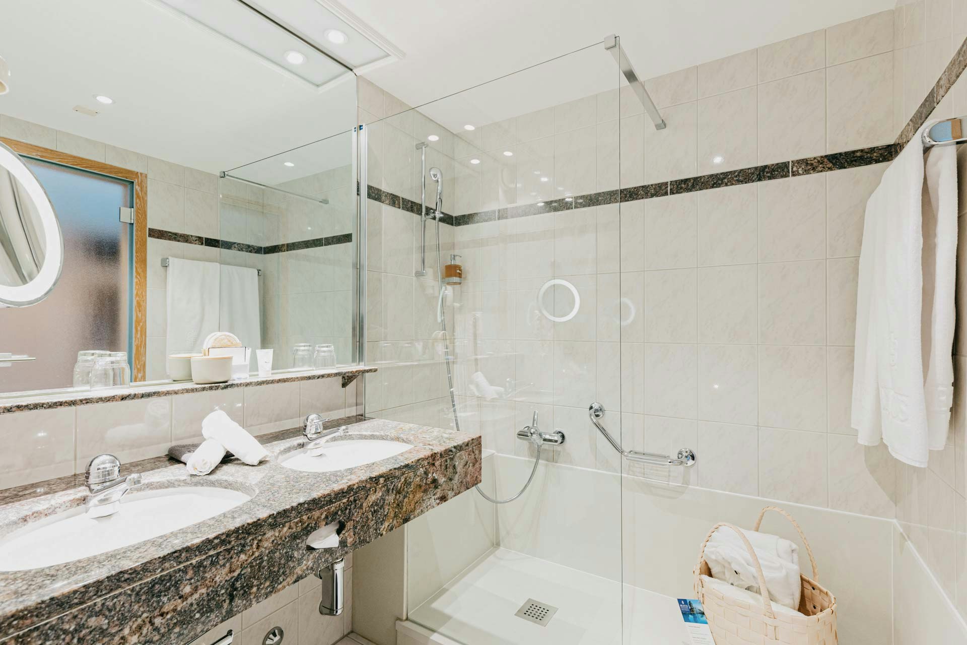 Bathroom with two washbasins and marbled shelf, mirror above, shower with glass panel