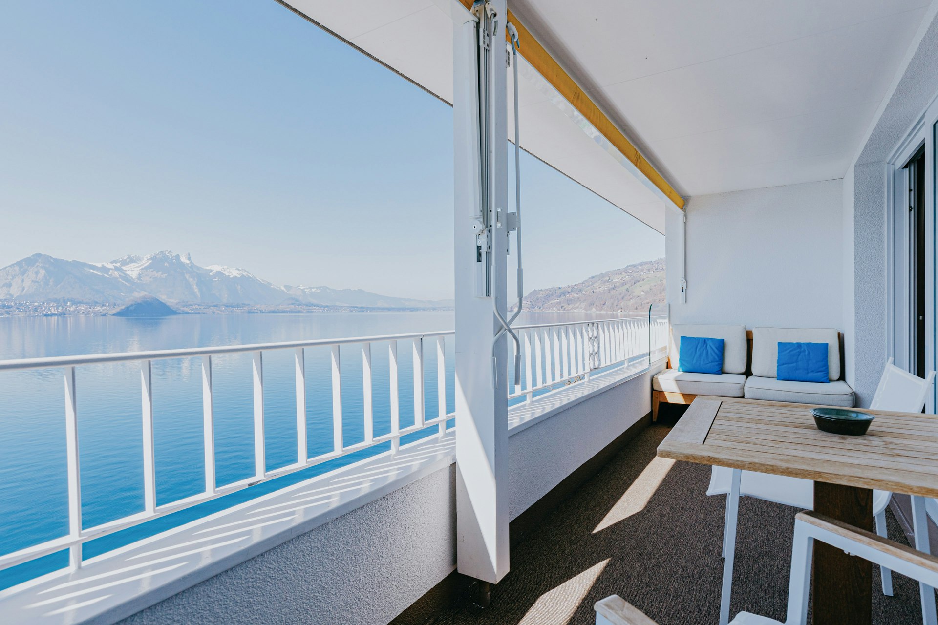 Balkon mit Tisch und Sofa, Blick auf einen blauen See und Berge