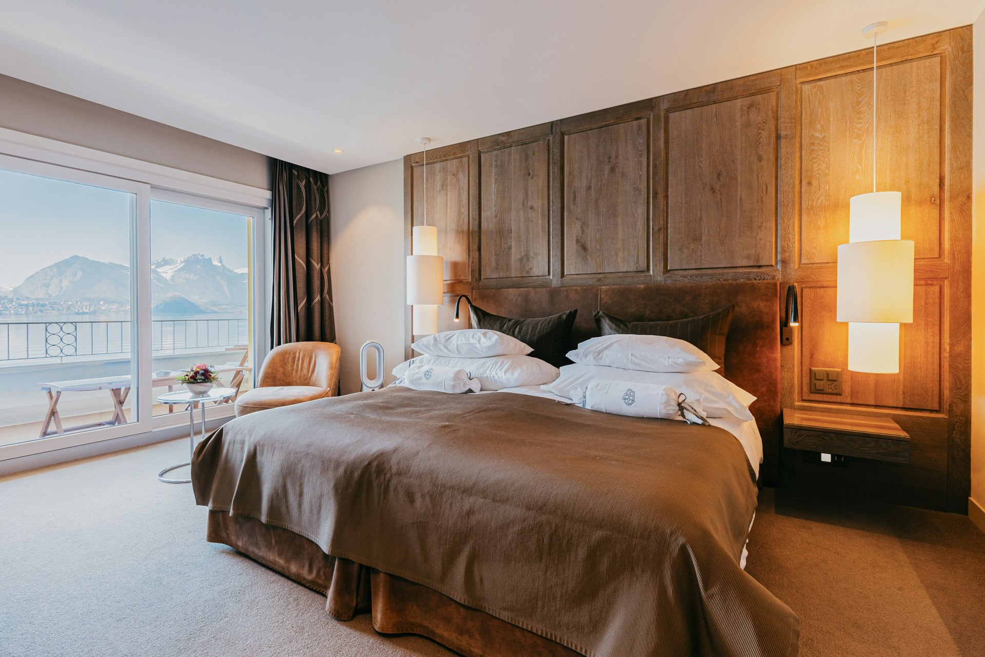 Chambre à coucher avec lit double, lambris en bois, deux lampes suspendues, grande fenêtre, derrière un balcon