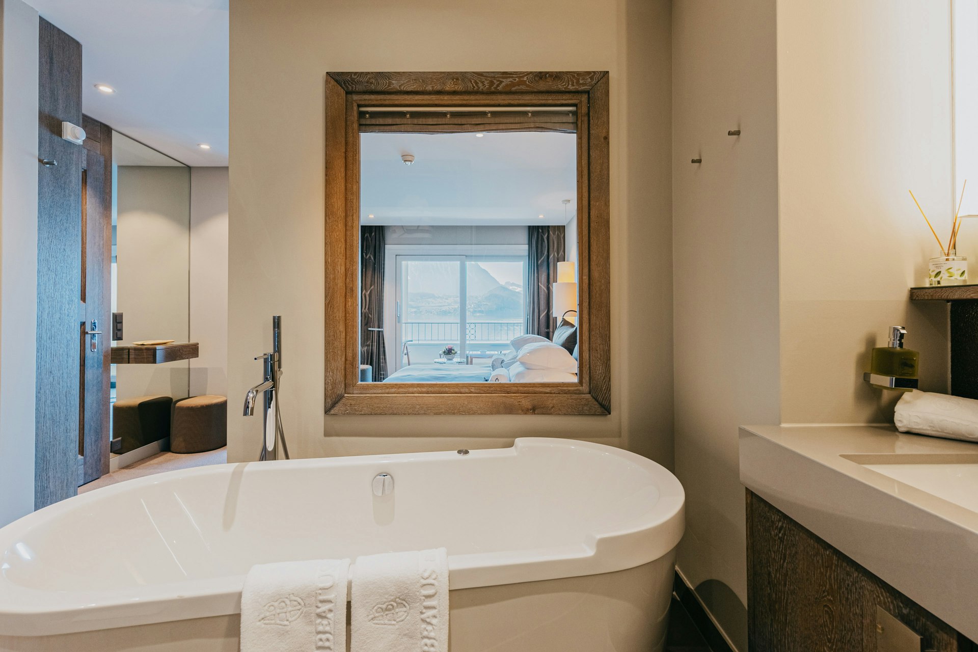 Salle de bain avec baignoire, fenêtre donnant sur une chambre voisine et lavabo