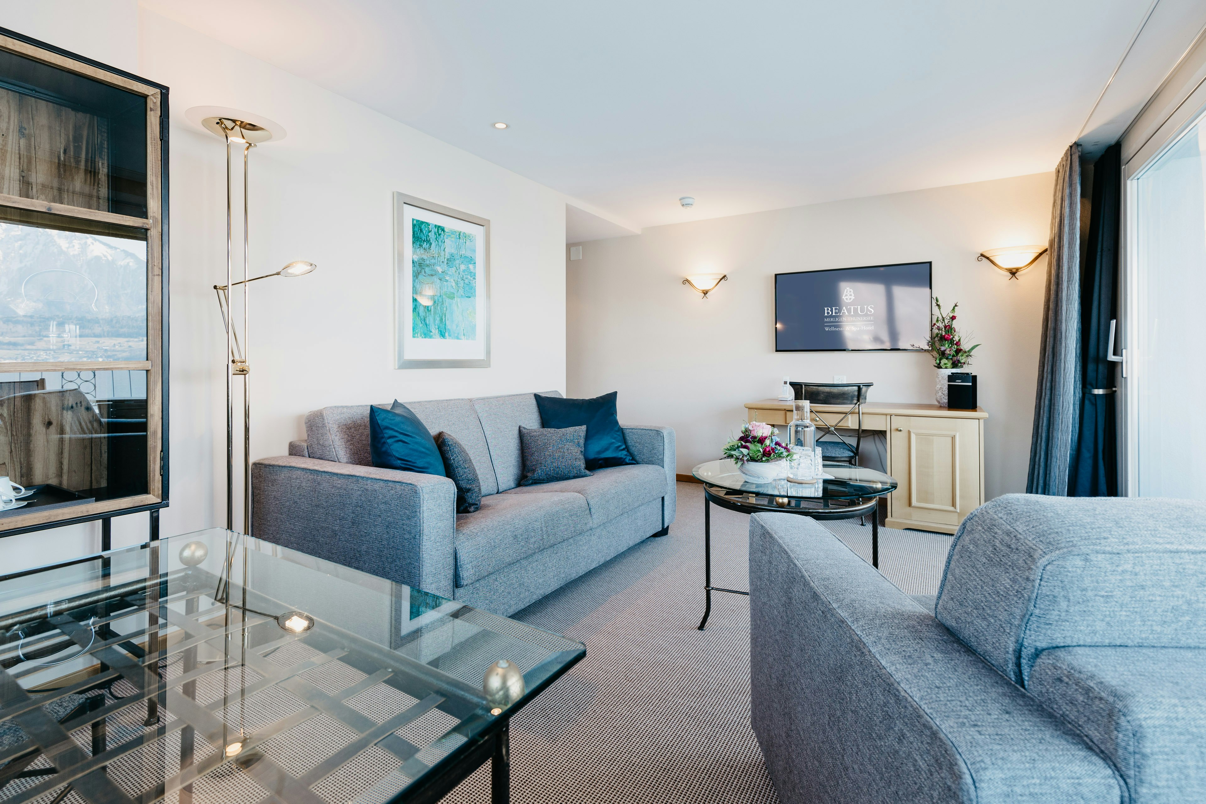 Wohnzimmer mit grauem Polstersessel und Sofa und zwei Glastischen