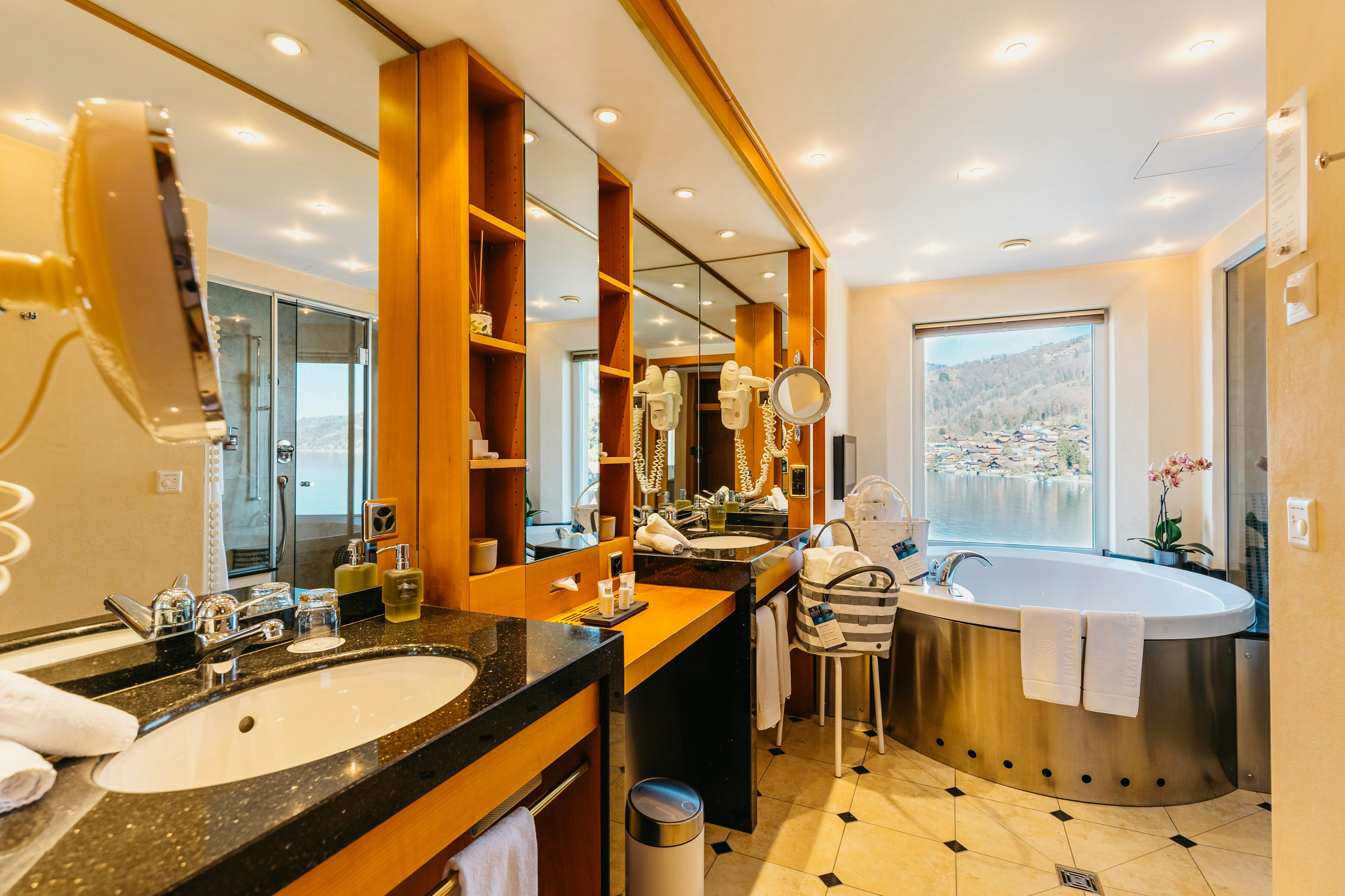 Badezimmer mit schwarz-weissem Fliesenboden, links ein Waschbecken, hinten eine Whirlwanne und ein Fenster mit Seeblick