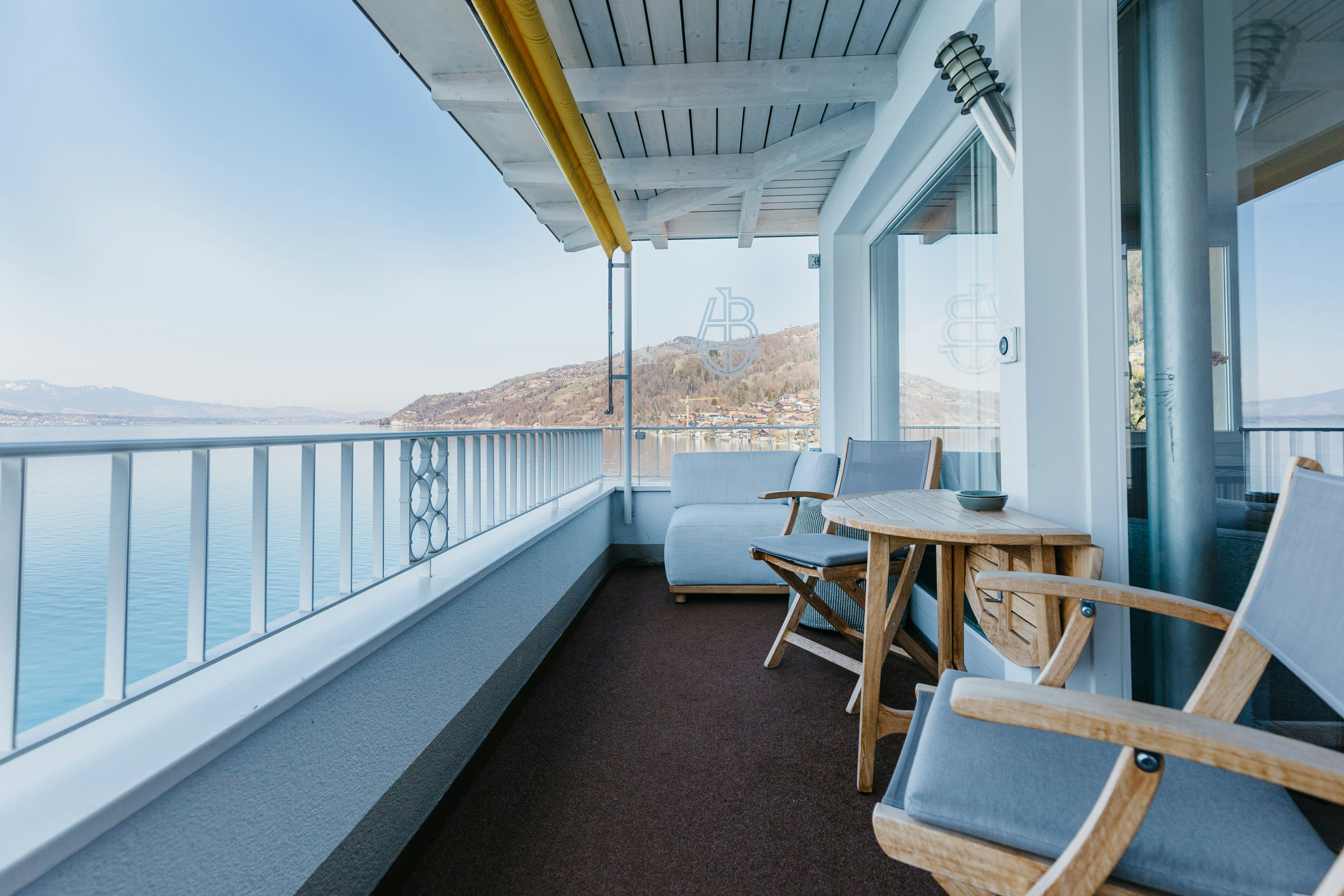 Grosser Balkon mit zwei Stühlen und einem Tisch, links der See