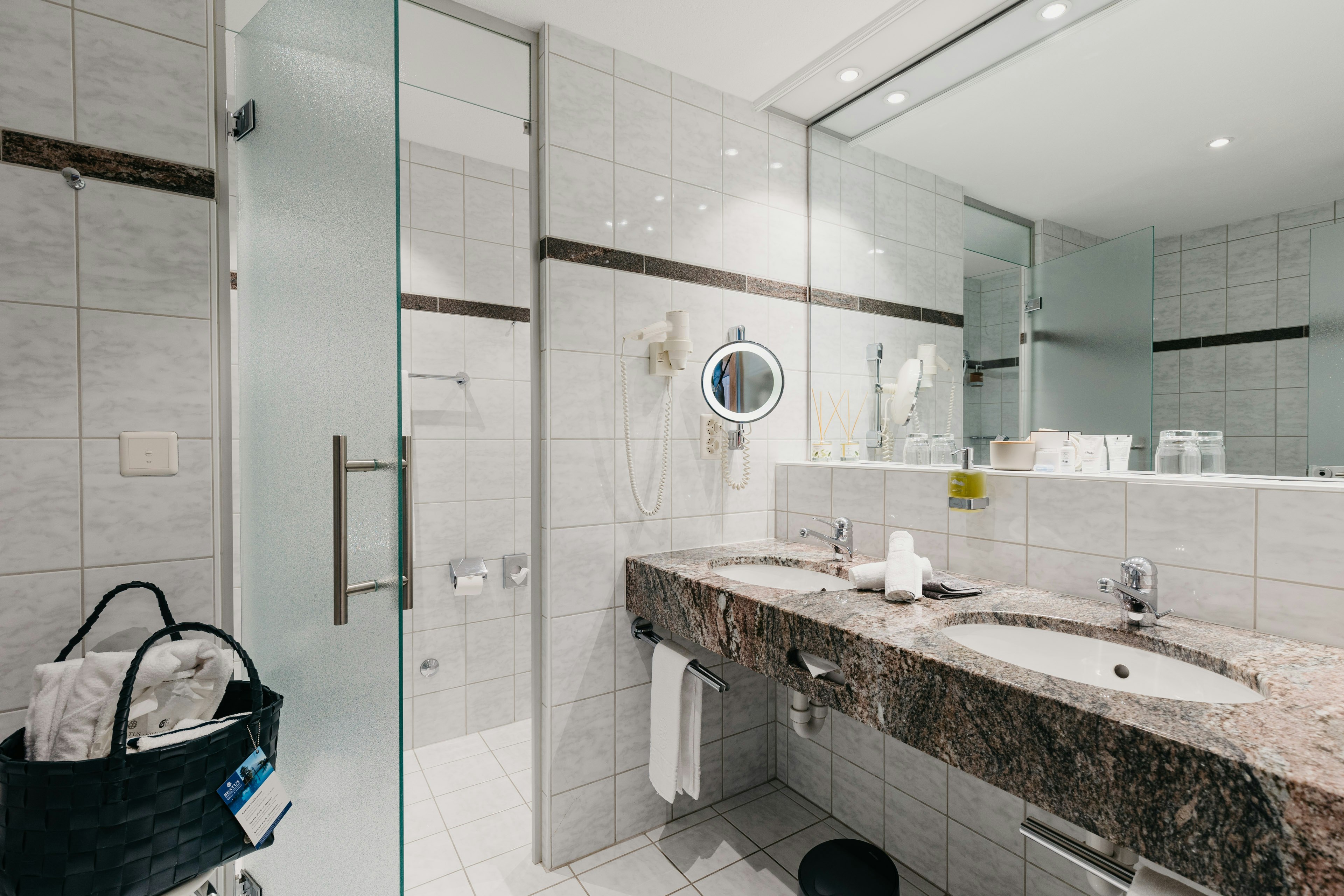 Badezimmer mit zwei eingebauten Waschbecken und grossem Spiegel, Glastür zum WC, Badetasche