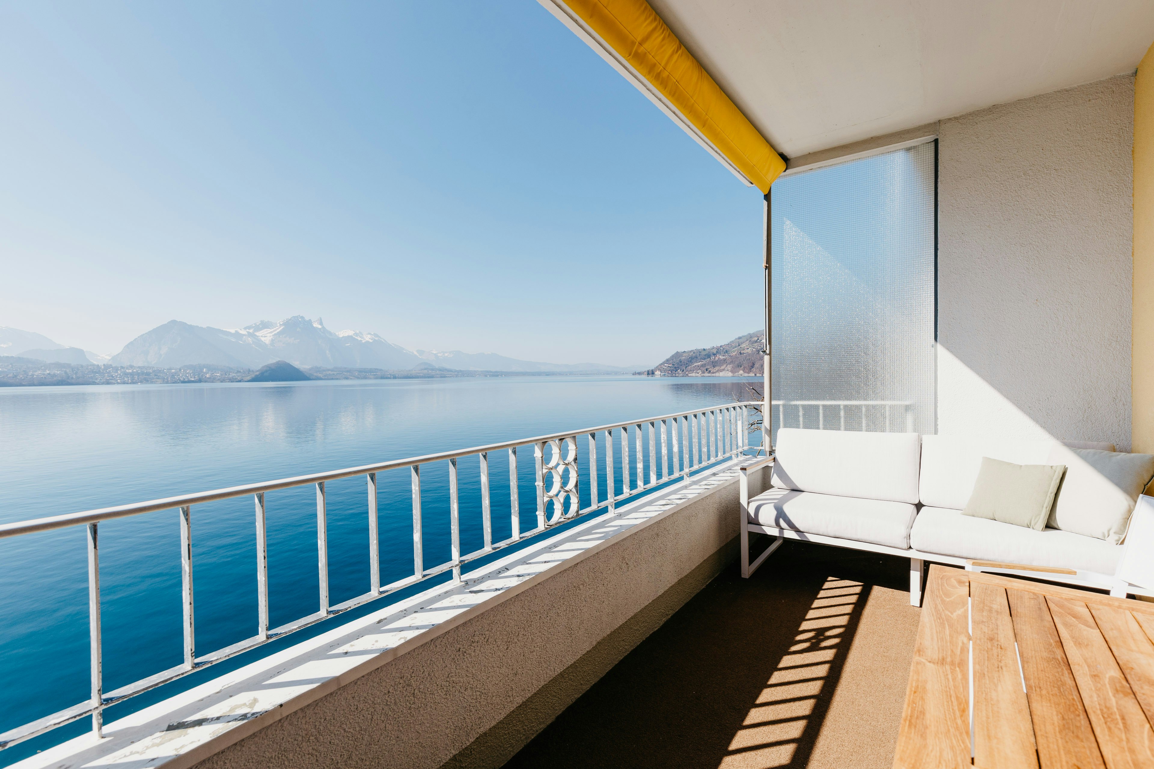 Balkon mit Holzboden, hinten ein weisses Sofa, links der blaue See