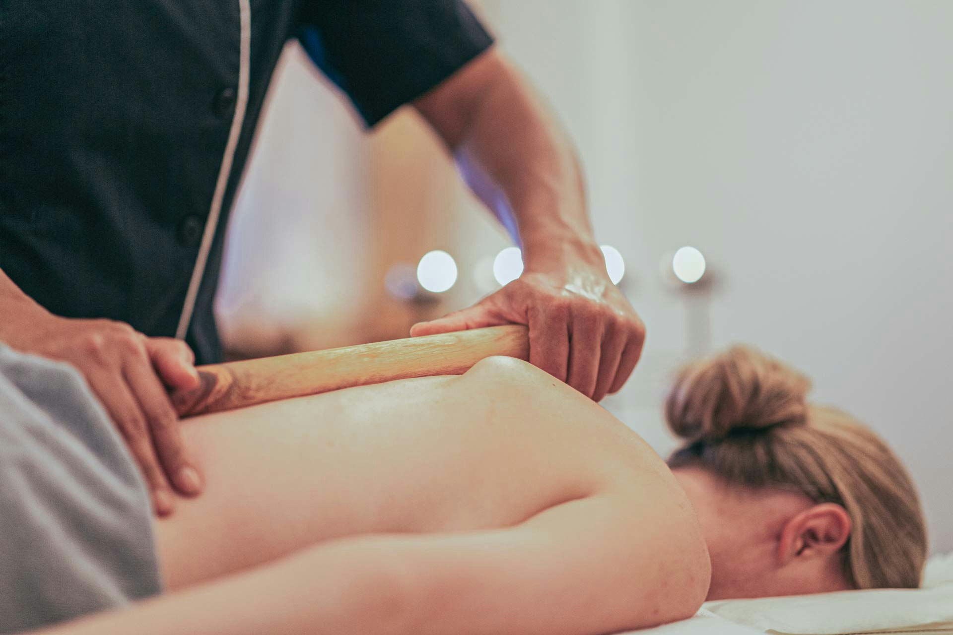 Eine Frau liegt auf dem Bauch auf einer Massageliege und wird mit einem Zirbenstock massiert