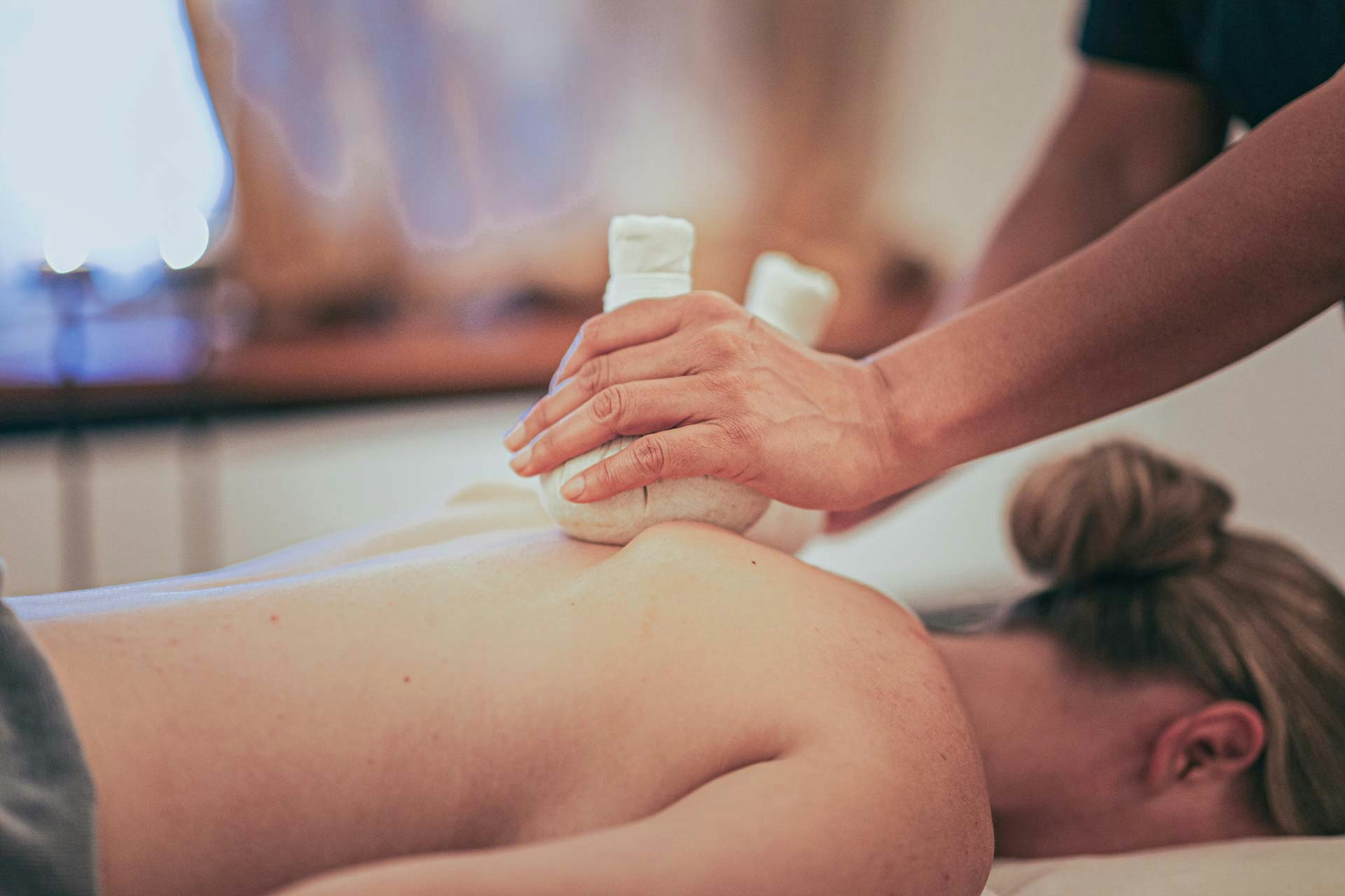 Eine Frau liegt auf dem Bauch auf einer Massageliege und wird mit Kräuterstempeln massiert