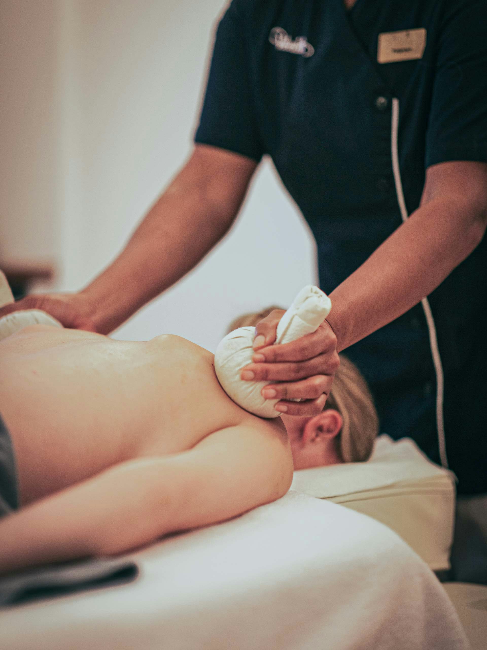 Pantai Luar massage at Hotel BEATUS A woman lies on her stomach on a massage table and is massaged with herbal stamps